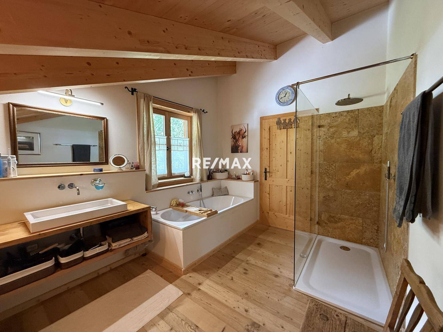 Geräumiges Badezimmer mit Badewanne, Duschkabine, Holzwaschtisch und Holzbalkendecke.