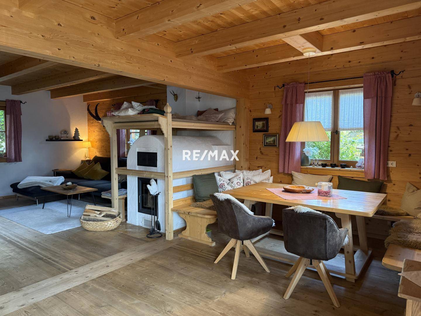 Gemütlicher Wohn-Essbereich im alpinen Stil mit Kachelofen, Holzbalkendecke und Esstisch.