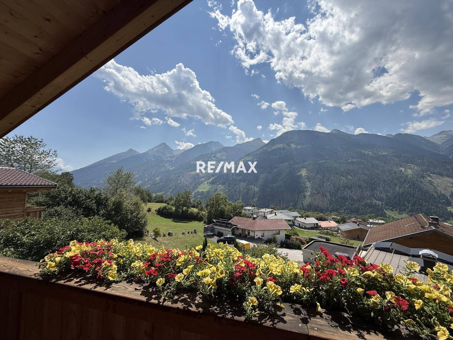 Malerischer Bergblick vom Balkon mit bunten Blumenkästen unter blauem Himmel.