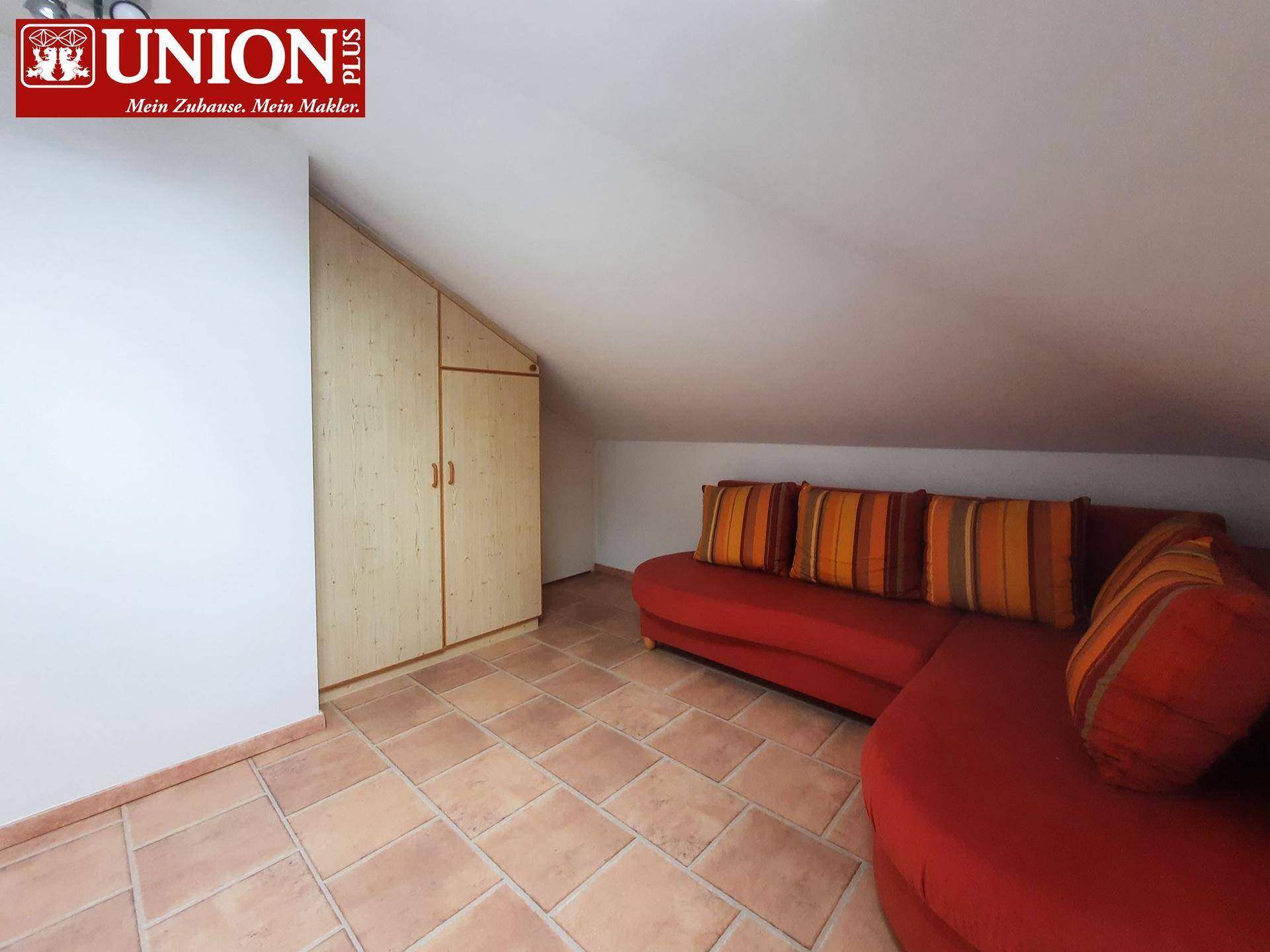 Gemütlicher Wohnbereich unter Dachschräge mit Terrakottafliesen und rotem Sofa.