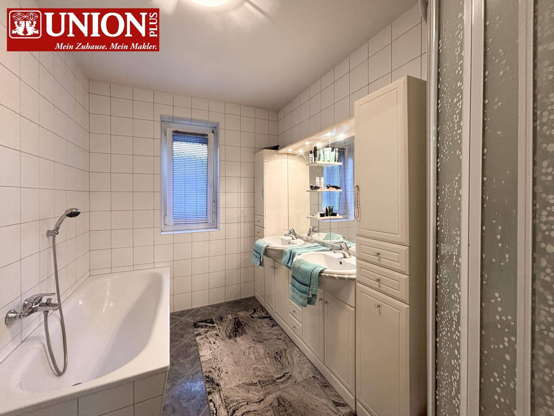 Gefliestes Badezimmer mit Badewanne, separater Dusche, Doppelwaschbecken und Spiegelschrank.