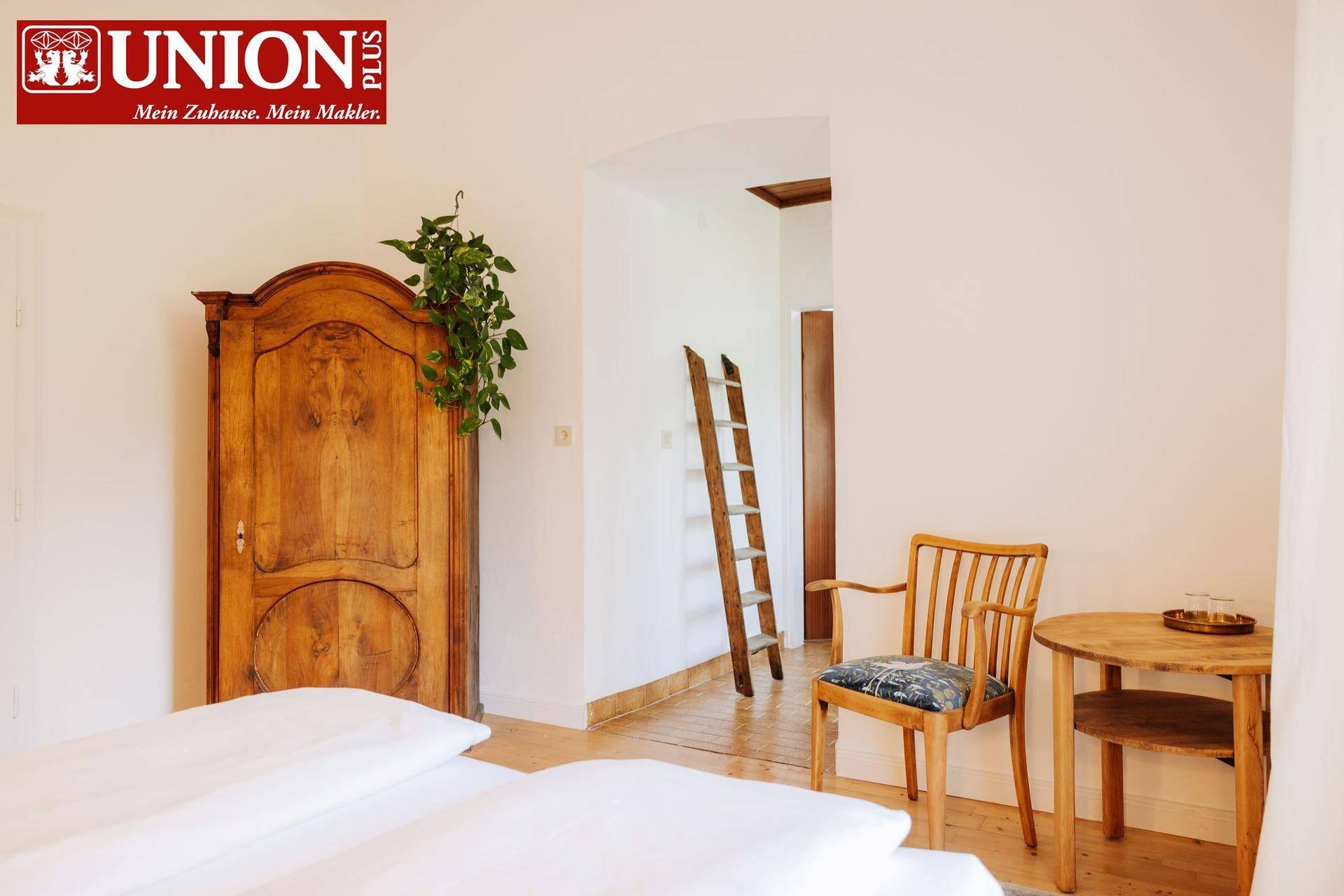 Schlafzimmer mit einem antiken Holzschrank, einfacher Einrichtung und einem Blick in den Flur.