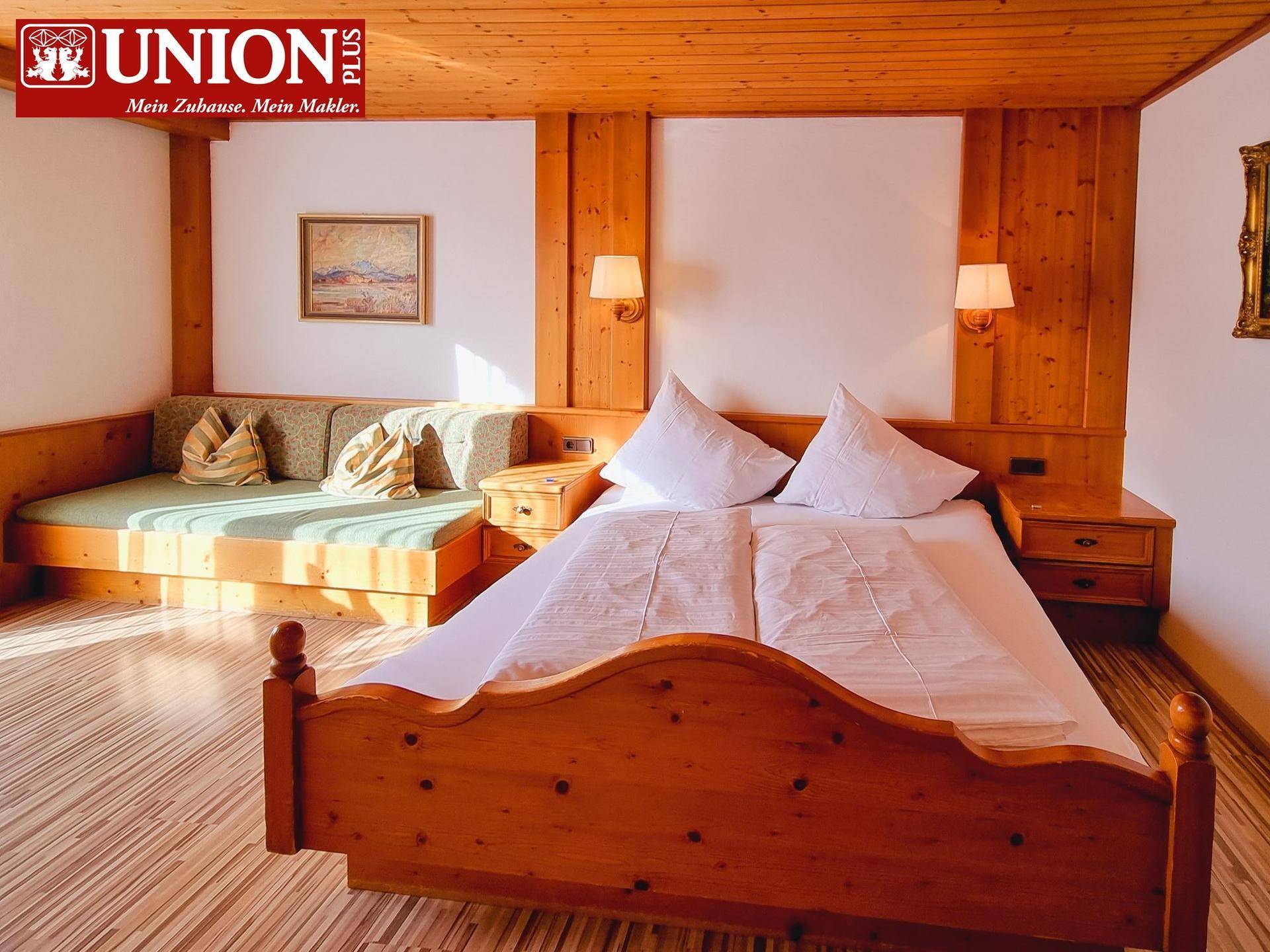 Helles Schlafzimmer im Landhausstil mit Holzbett, Holzvertäfelung und gemütlicher Sitzecke.