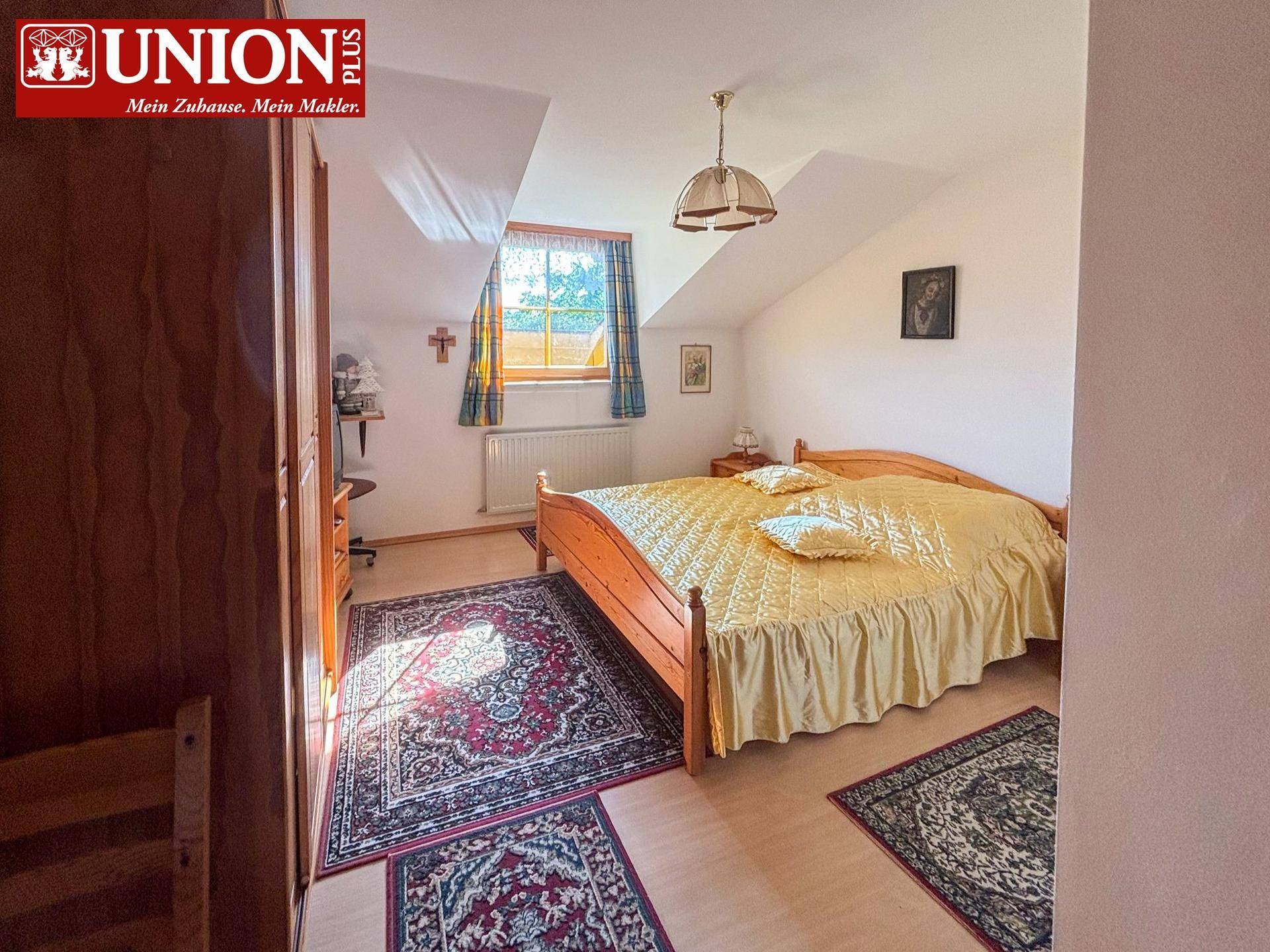 Gemütliches Schlafzimmer im Dachgeschoss mit Doppelbett, Teppichen und schrägen Decken.