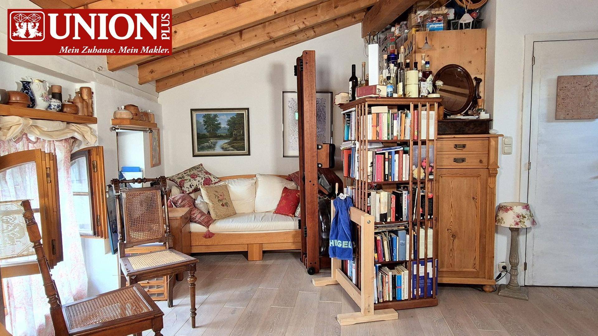 Wohnbereich mit Sofa, Bücherregal und Holzbalkendecke, bietet eine gemütliche Atmosphäre.
