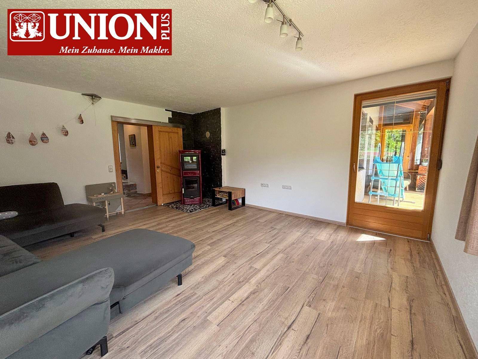 Helles Wohnzimmer mit Laminatboden, gemütlichem Sofa und Zugang zu einem Wintergarten oder Balkon.