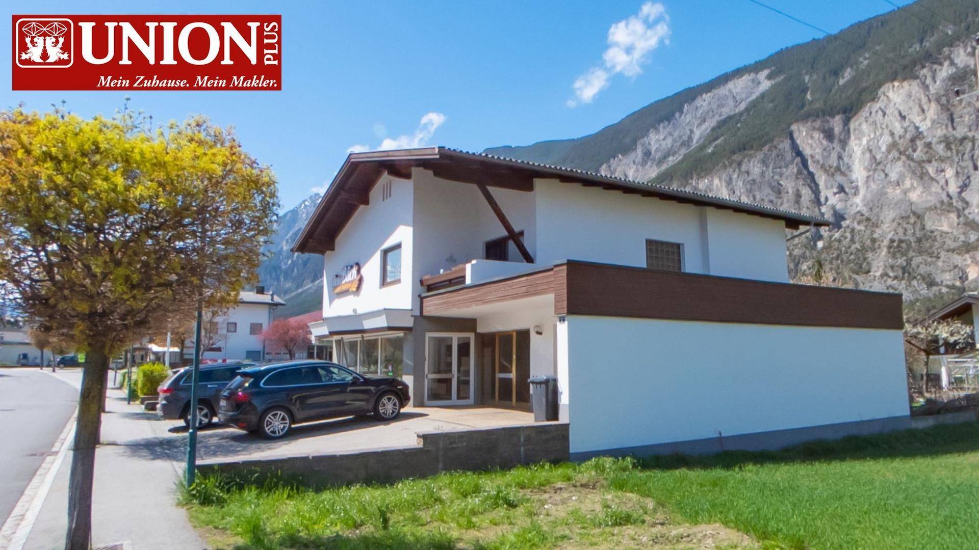 Seitenansicht des Gebäudes mit traditionellen Holzelementen und Blick auf die umliegende Berglandschaft.