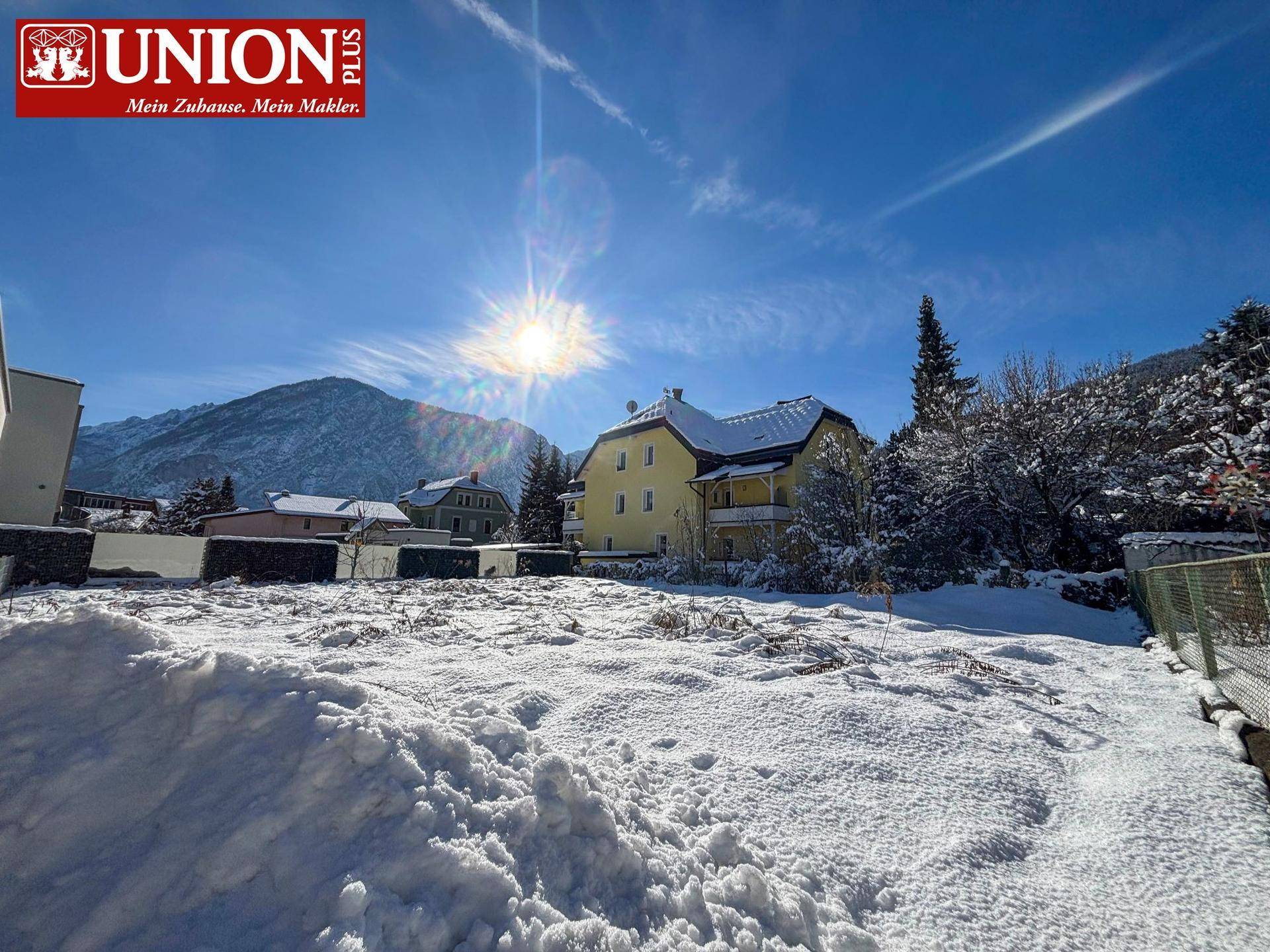 Gelbes Haus in winterlicher Umgebung mit schneebedeckten Bergen und klarem, sonnigem Himmel.