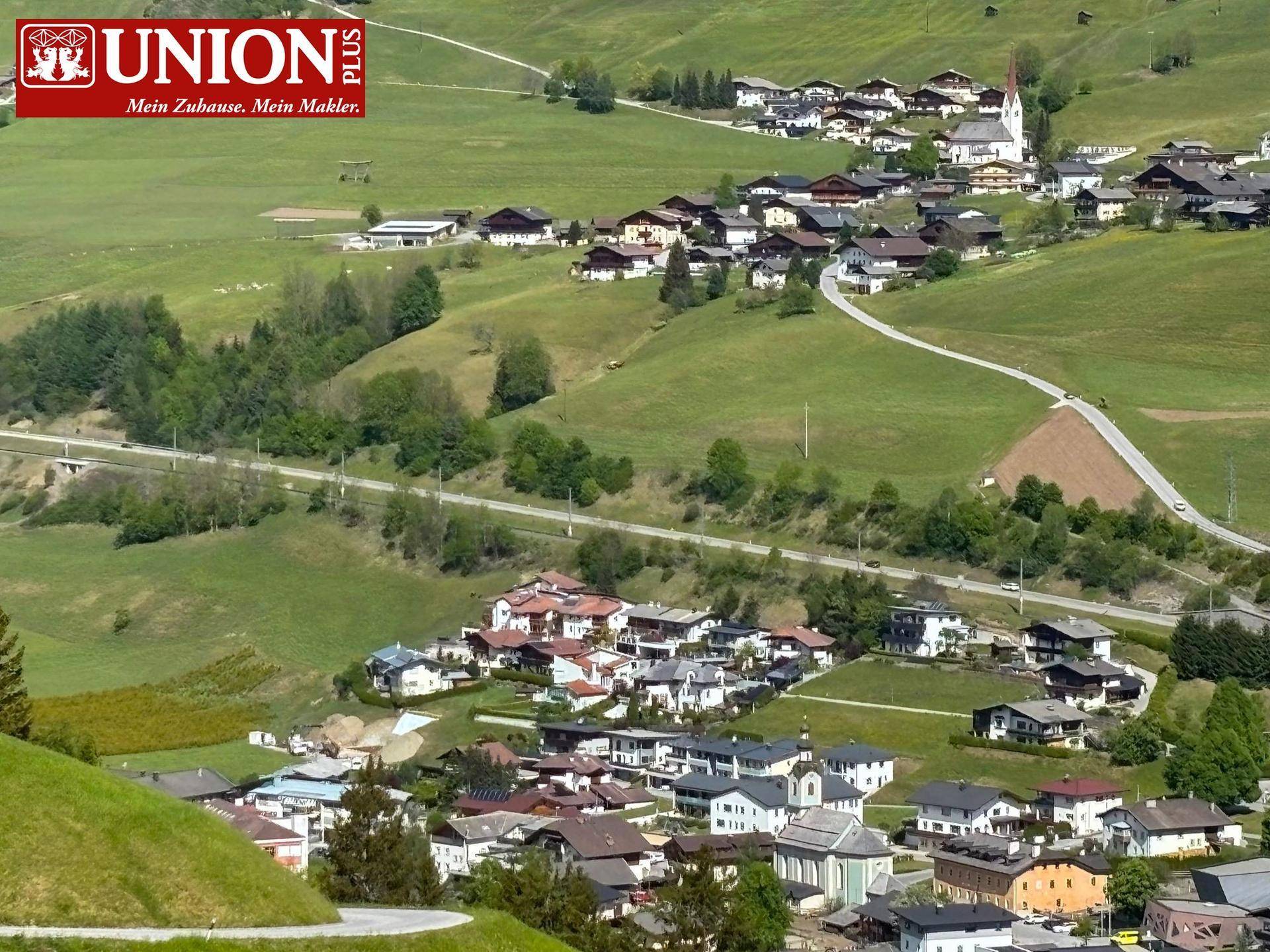 Luftaufnahme eines charmanten Dorfes eingebettet in eine grüne alpine Landschaft mit vielen Häusern.