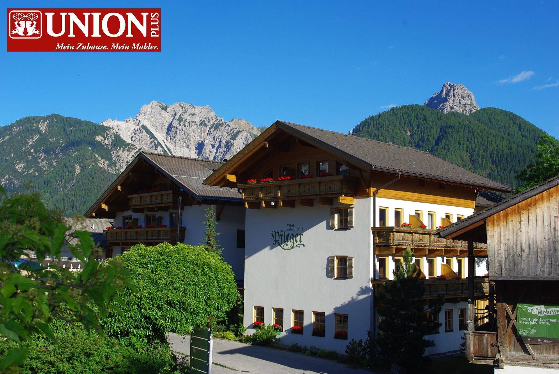 Traditionelles Gebäude mit Holzbalkonen und Bergblick unter strahlend blauem Himmel in alpiner Landschaft.