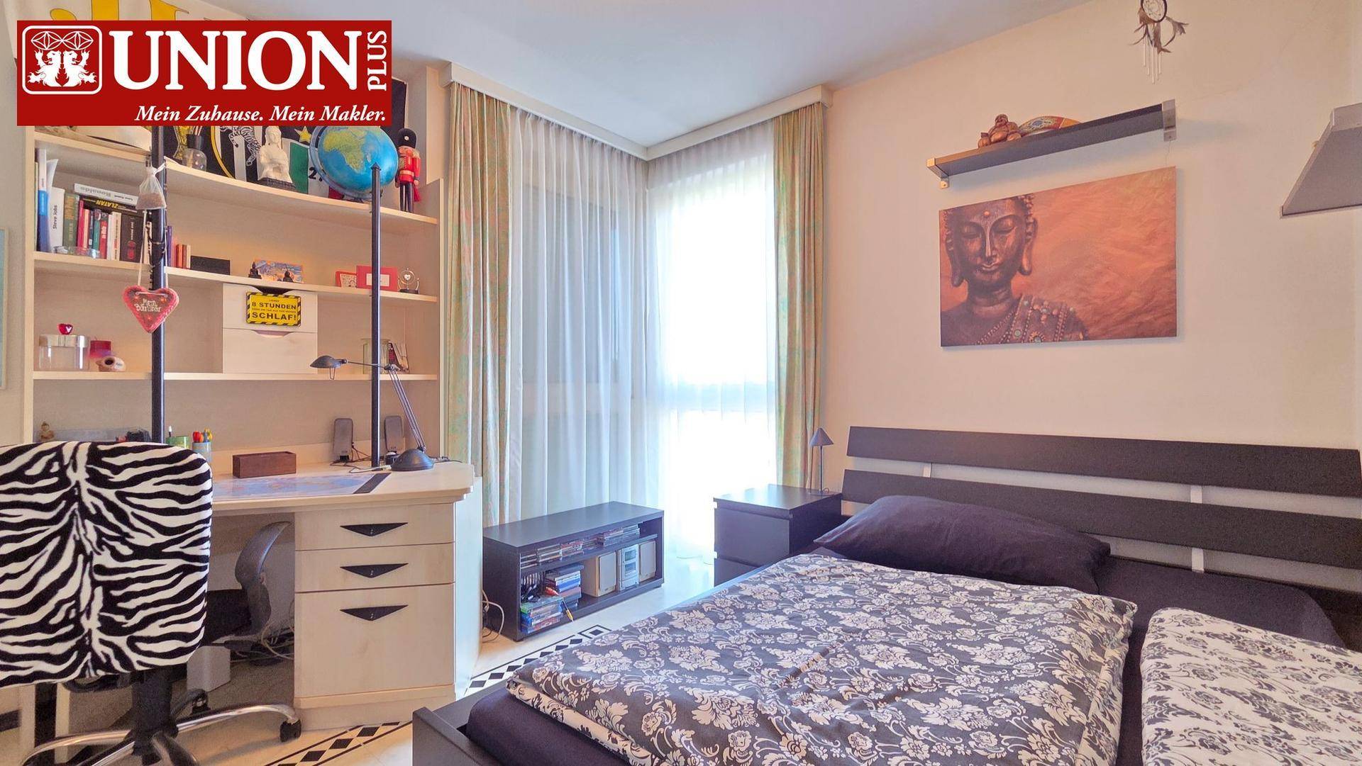 Helles Schlafzimmer mit Schreibtisch, Regal und Blick ins Grüne durch das Fenster.