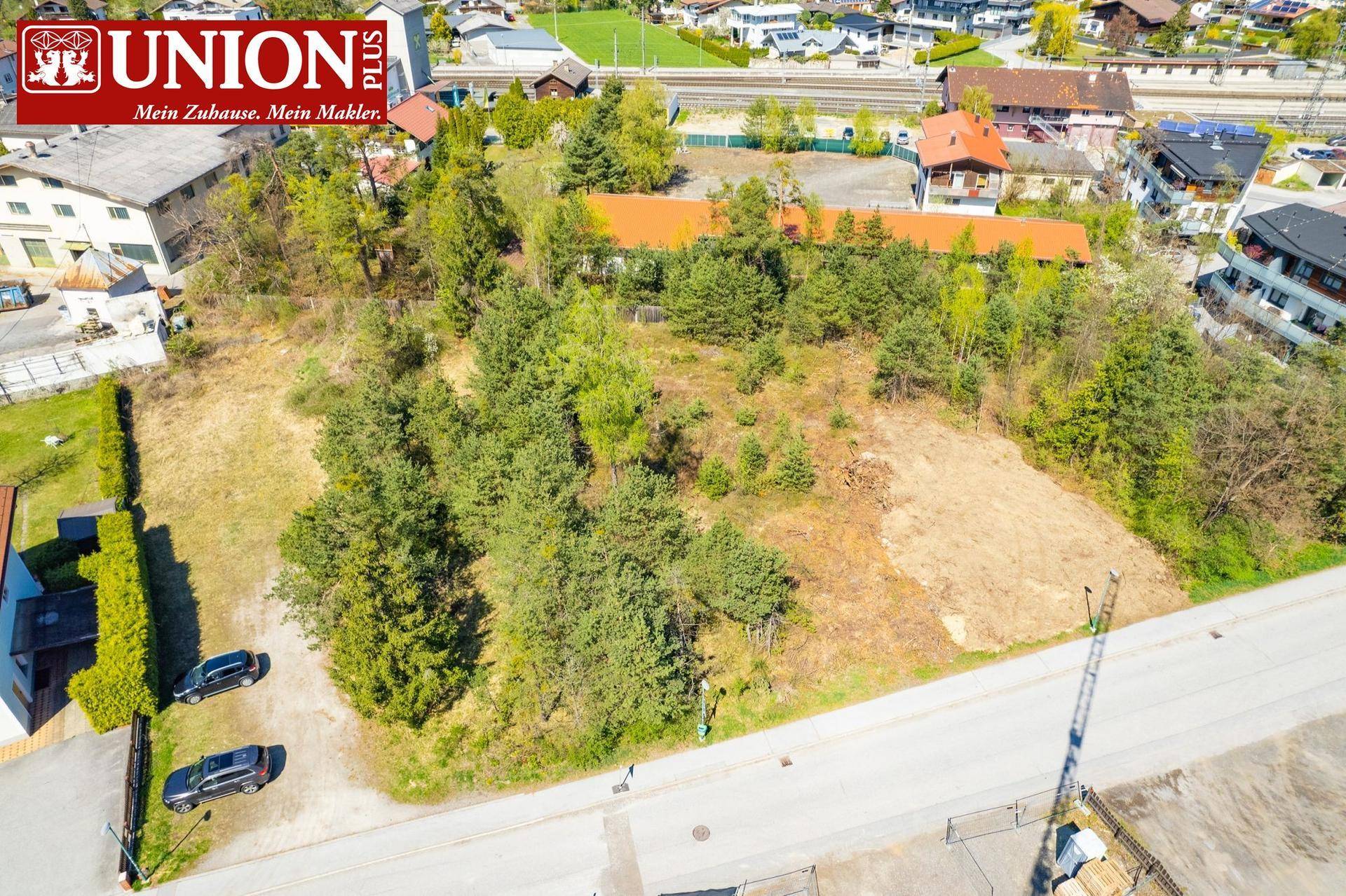 Luftaufnahme eines unbebauten Grundstücks mit angrenzender Straße und umliegenden Gebäuden.