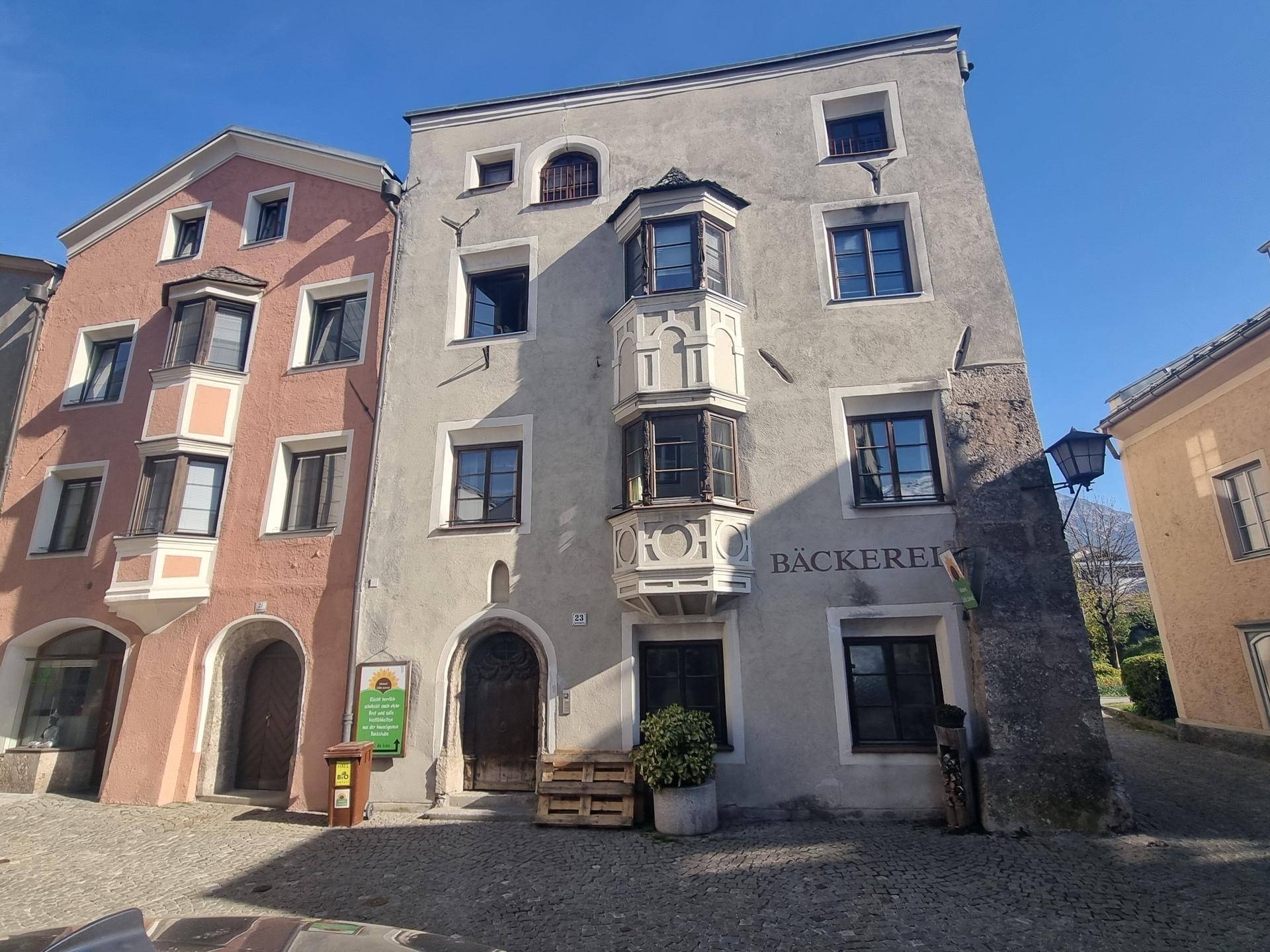 Historisches Gebäude mit markanten Erkerfenstern und einer Bäckerei im Erdgeschoss an einer Kopfsteinpflasterstraße.