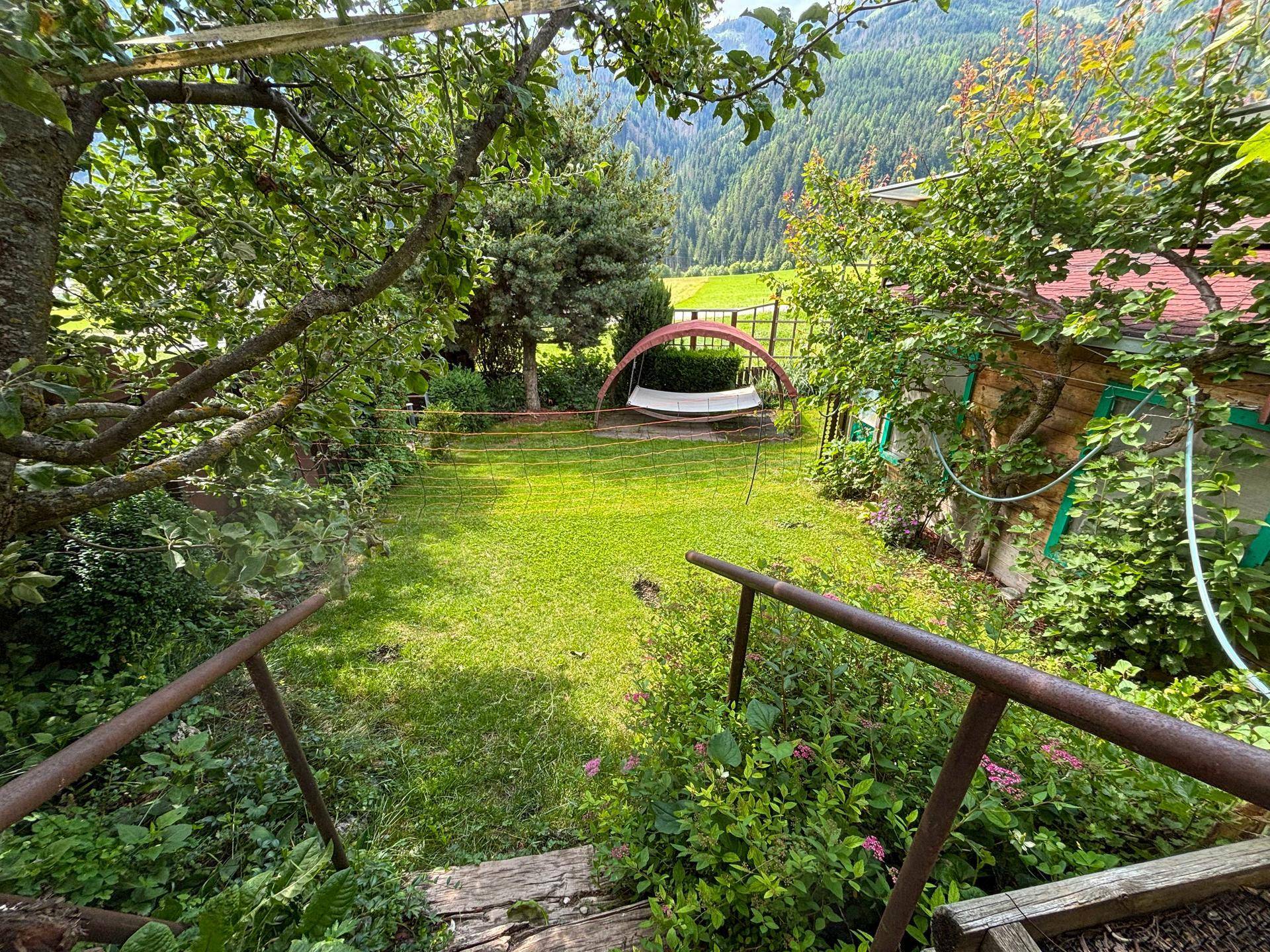 Malerischer Garten mit Rasenfläche, Obstbäumen und einer Schaukelbank, eingebettet in eine grüne Landschaft.