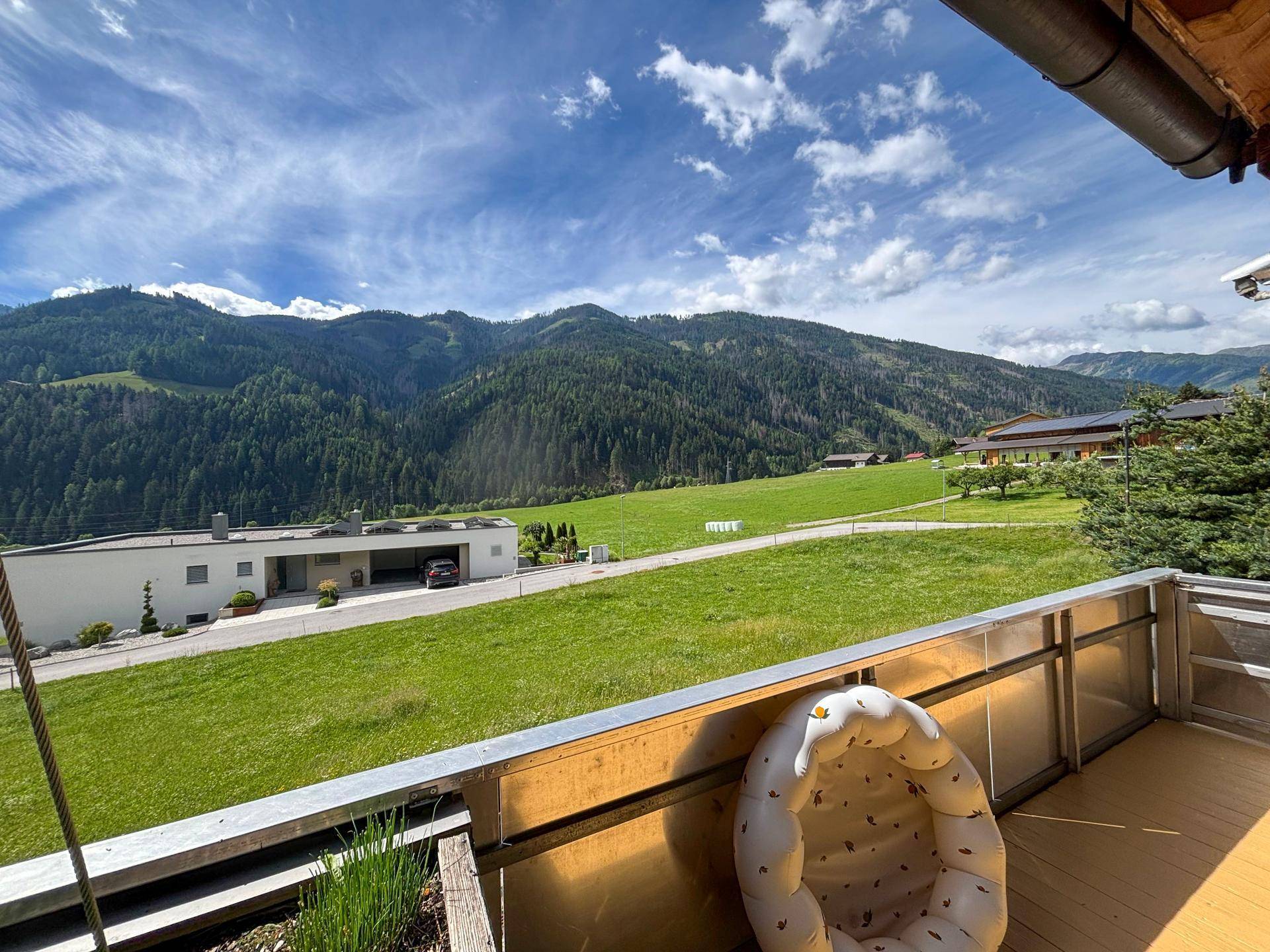 Balkon mit weitem Blick auf grüne Wiesen und die umliegende Berglandschaft unter blauem Himmel.