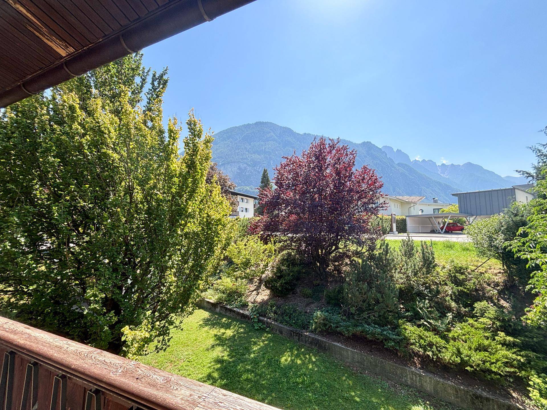 Panoramablick vom Balkon auf die umliegende Berglandschaft und grüne Bäume unter blauem Himmel.