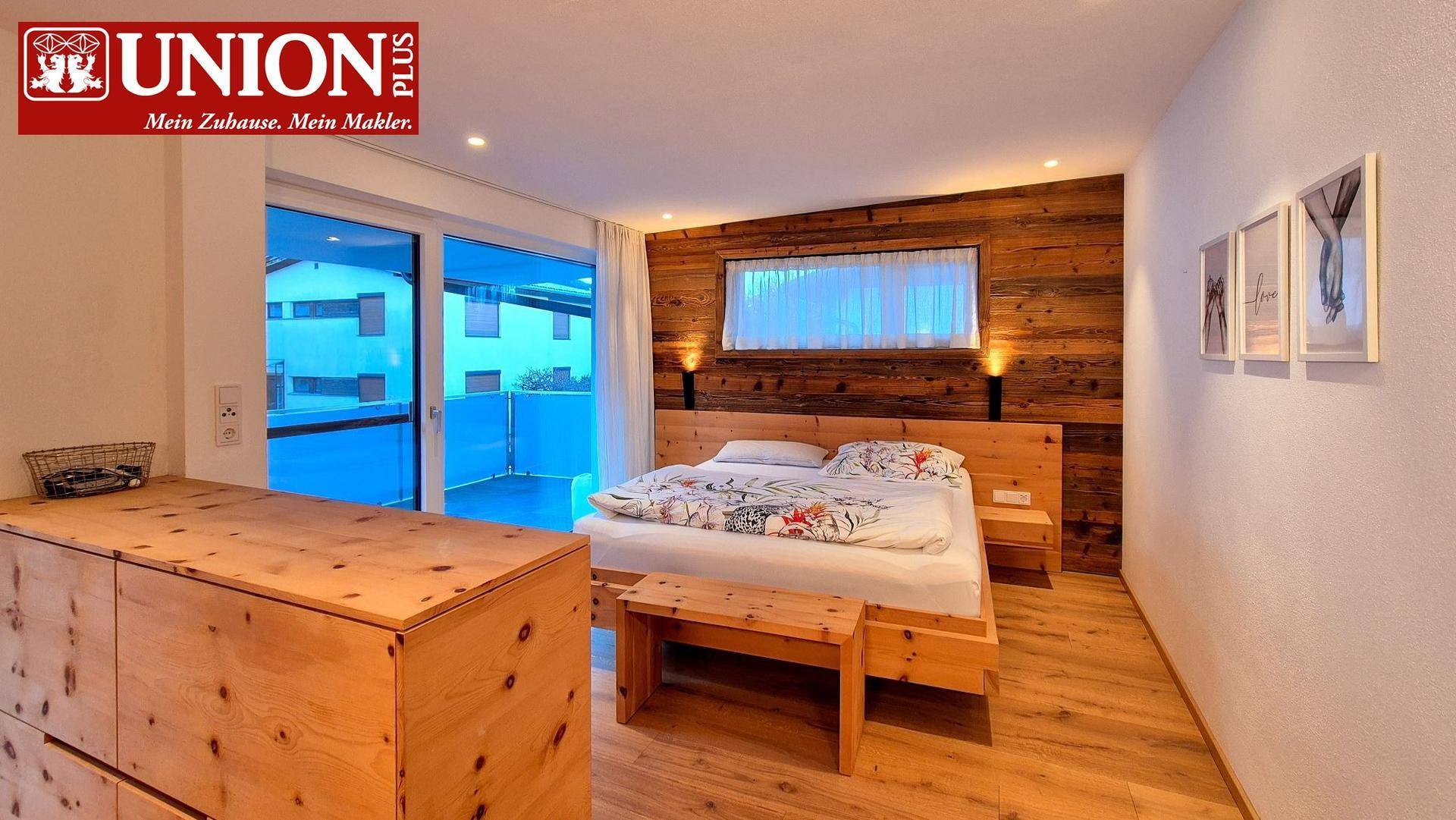 Helles Schlafzimmer mit Holzwandverkleidung, Holzbett und Zugang zu einem Außenbereich.