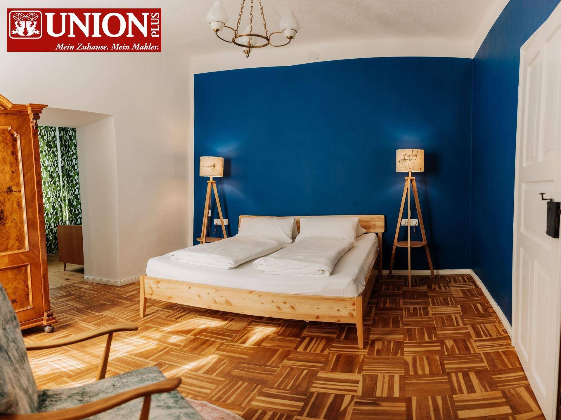 Gemütliches Schlafzimmer mit einem Holzbett, einer blauen Akzentwand und klassischem Parkettboden.