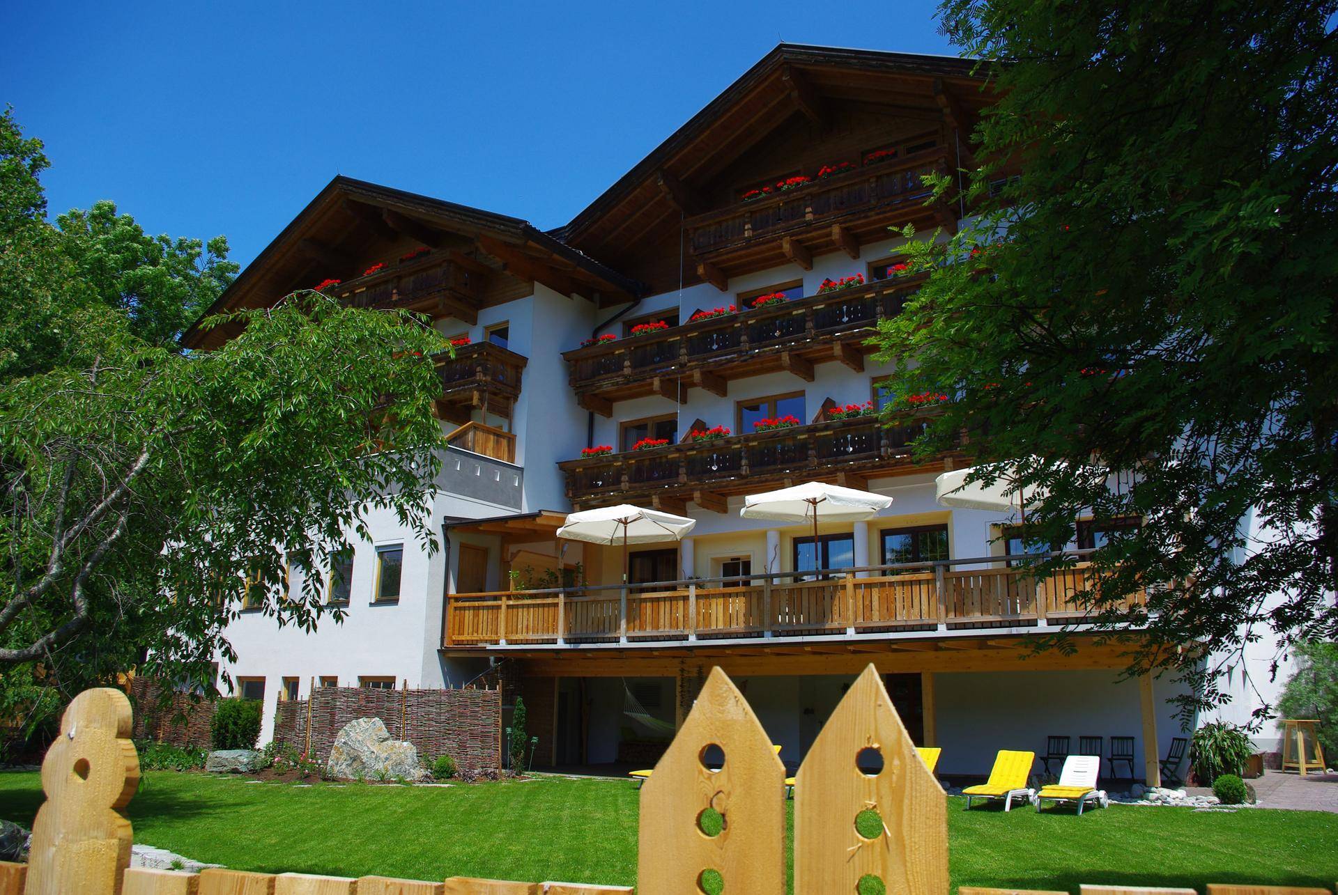 Charmantes Gebäude mit Holzbalkonen, einem gepflegten Garten und Liegestühlen unter blauem Himmel.