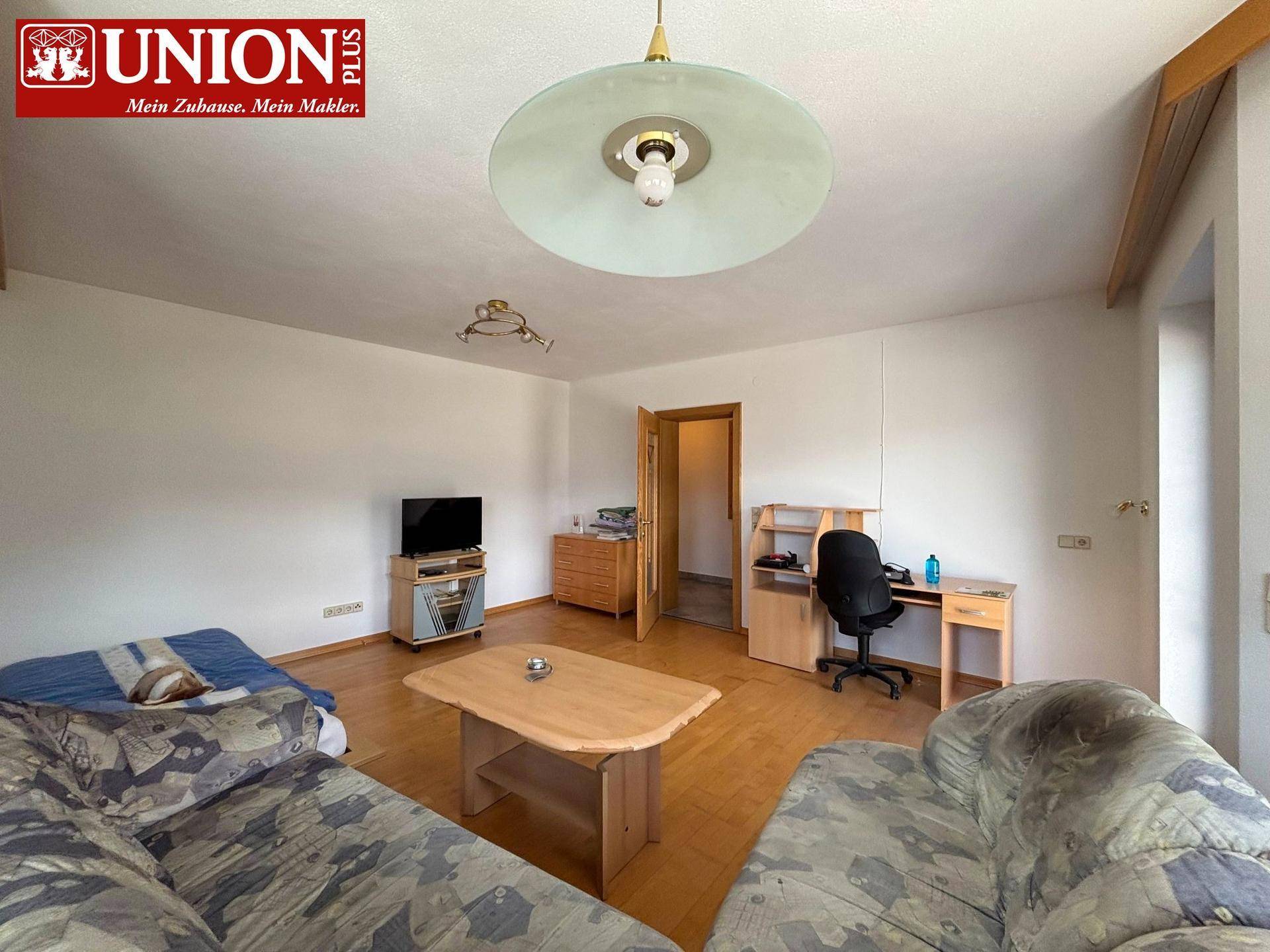 Gemütliches Wohnzimmer mit Sofa, Couchtisch, TV-Bereich und Arbeitsplatz.