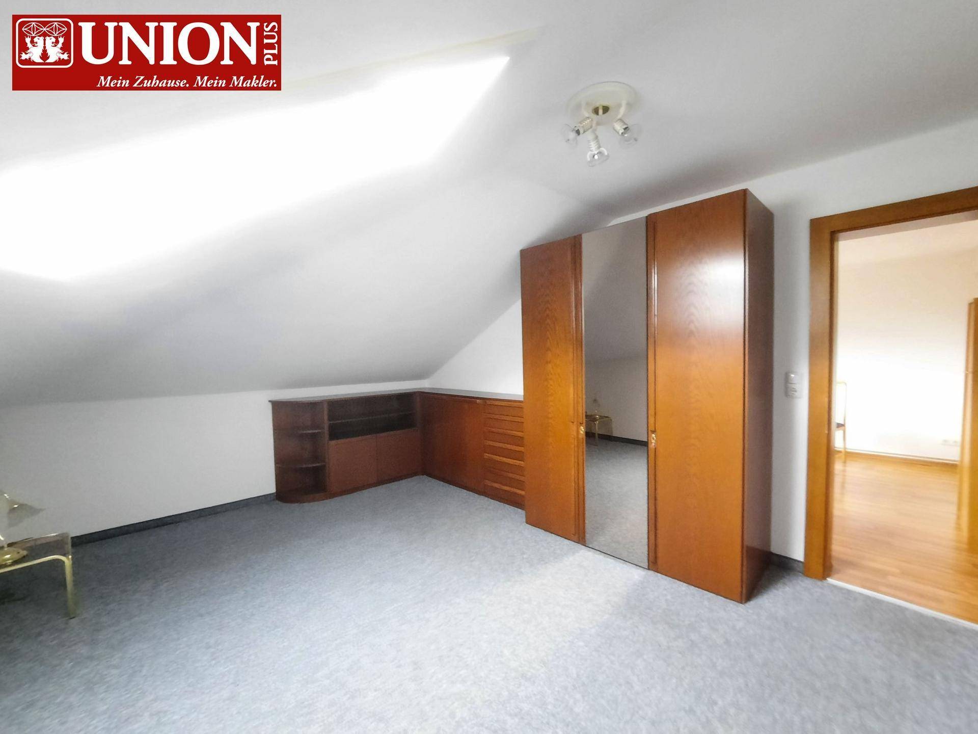 Schlafzimmer unter Dachschräge mit Teppichboden und großem Spiegelschrank.