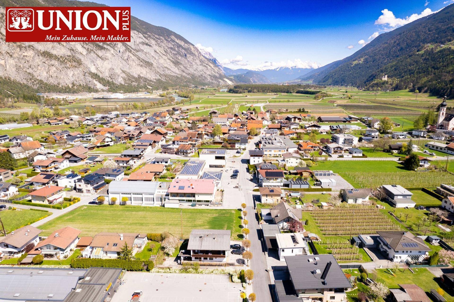 Weitläufige Luftaufnahme der Siedlung mit Blick auf die Alpen und die umliegende Naturlandschaft.