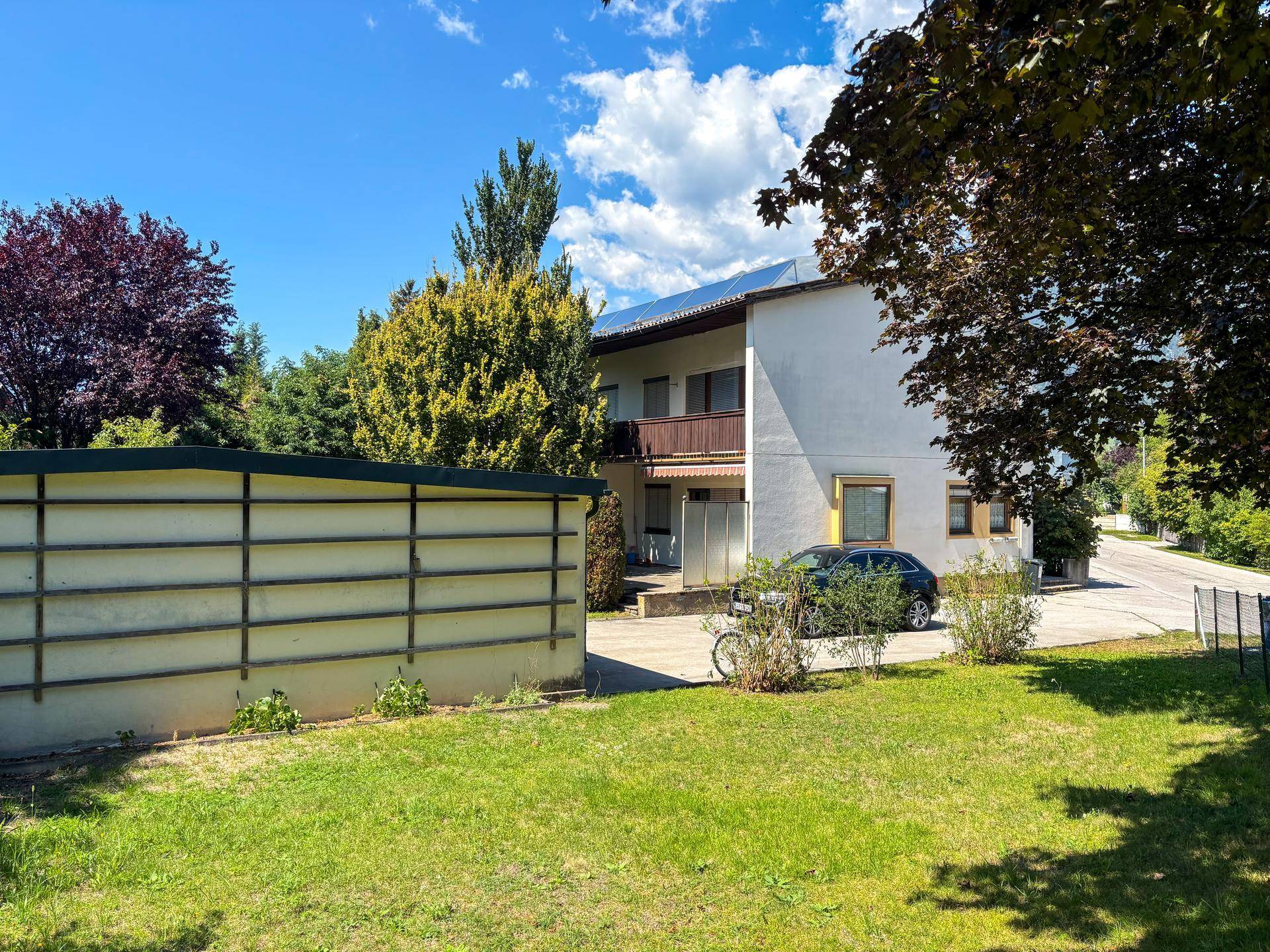 Mehrfamilienhaus mit Balkonen und Solaranlage auf dem Dach, umgeben von Grünflächen.