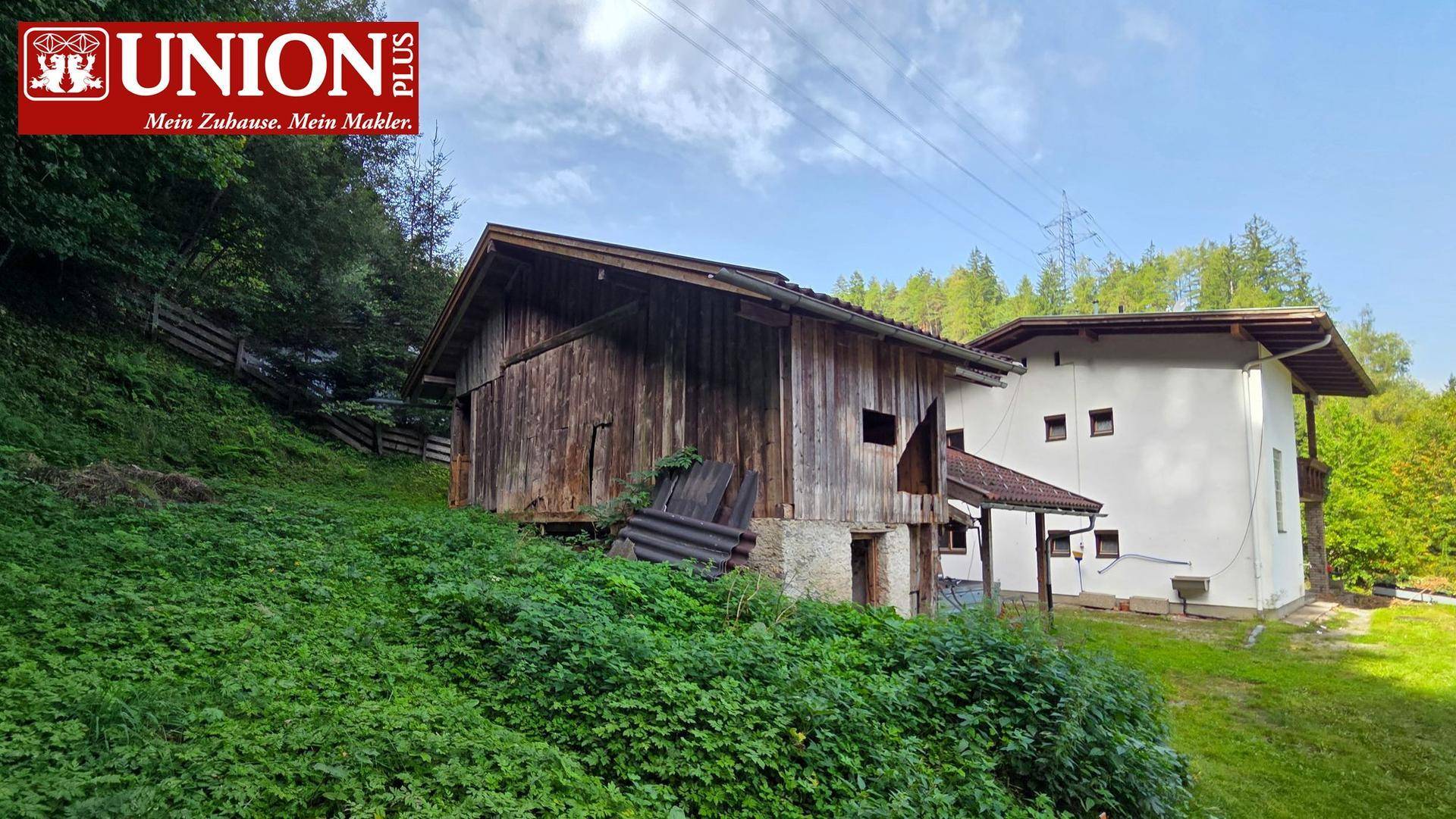 Wohnhaus und rustikale Holzscheune eingebettet in eine grüne, hügelige Landschaft.