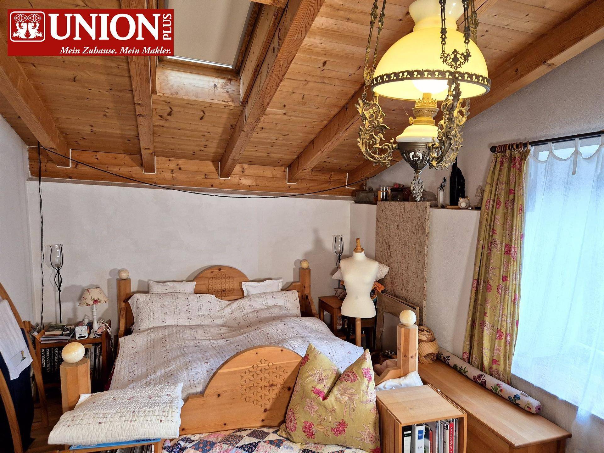 Gemütliches Schlafzimmer mit Holzbalkendecke, traditionellem Holzbett und viel natürlichem Licht.