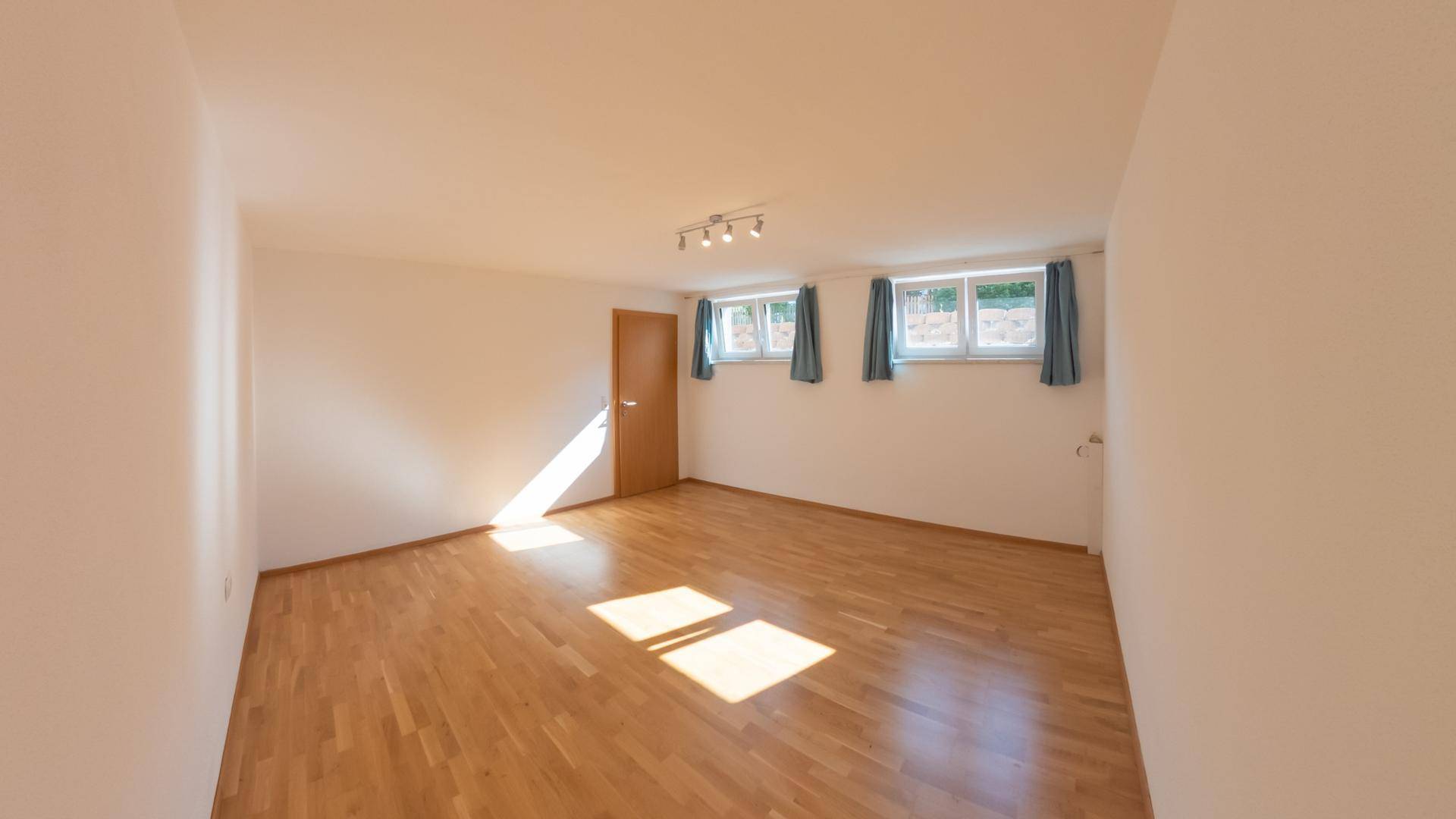 Geräumiger, unmöblierter Raum mit Parkettboden und mehreren Fenstern für viel Licht.