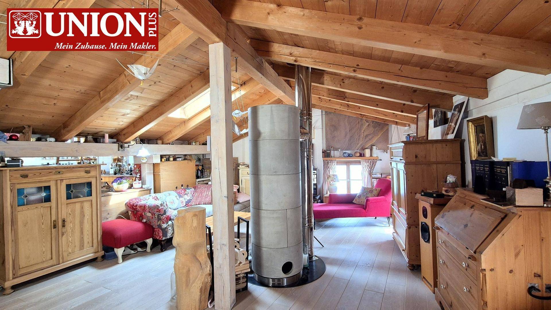 Geräumiges Wohnzimmer mit Holzbalken, Kaminofen und gemütlicher Sitzecke unter dem Dach.