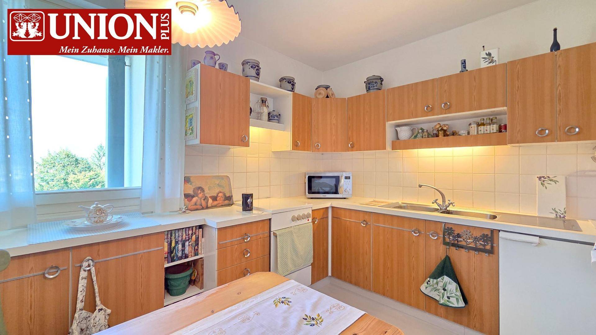 Funktionale Küche mit Holzfronten, weißen Fliesen, Fenster und integrierten Geräten.