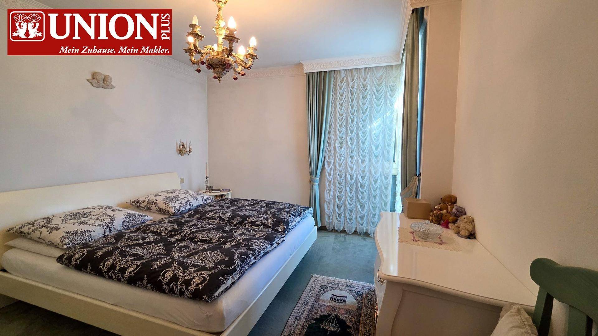 Schlafzimmer mit Doppelbett, Teppichboden, Kronleuchter und Zugang zu einem Balkon.