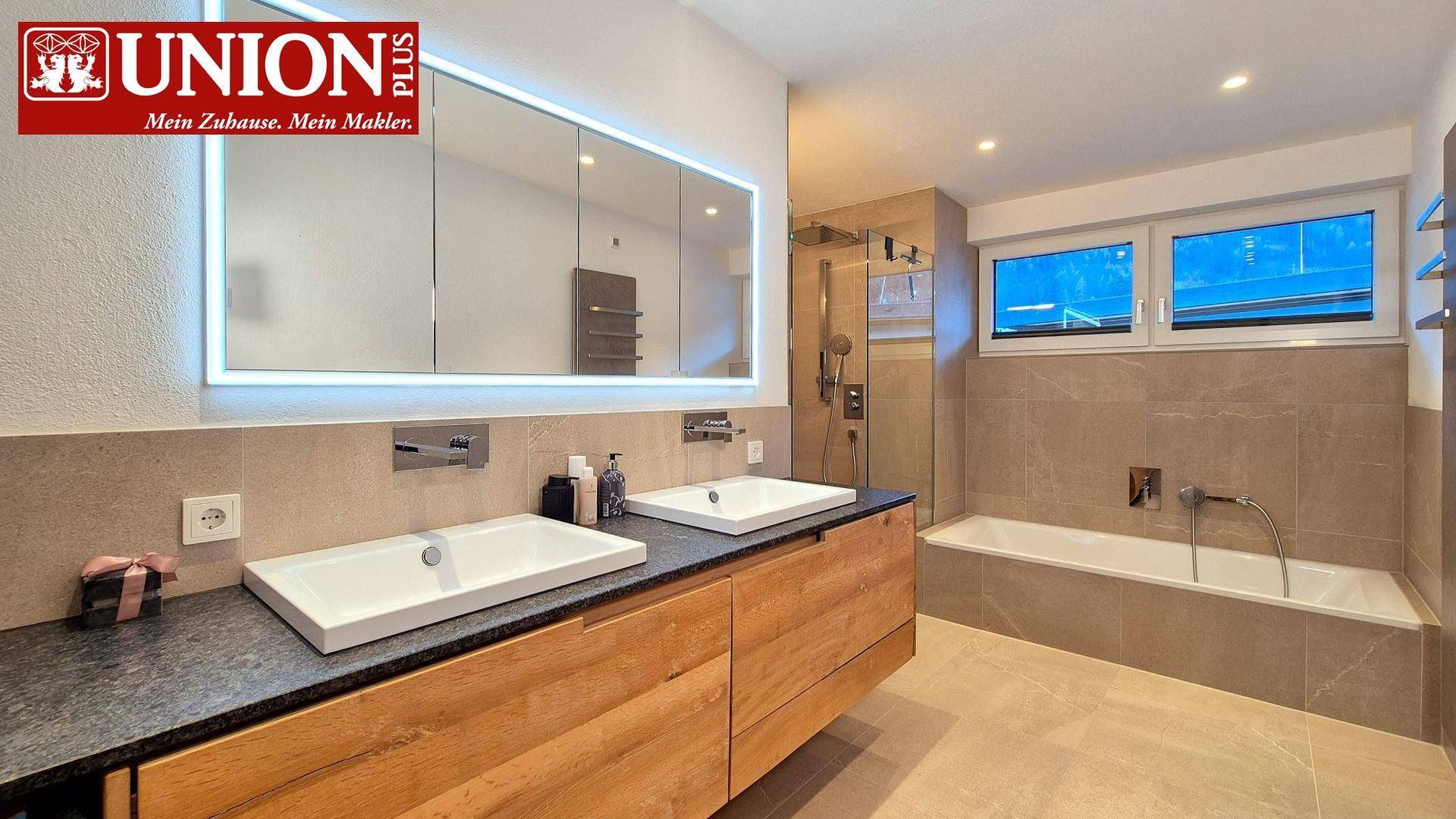 Modernes Badezimmer mit Doppelwaschbecken, großer Dusche und Badewanne, hell gefliest.