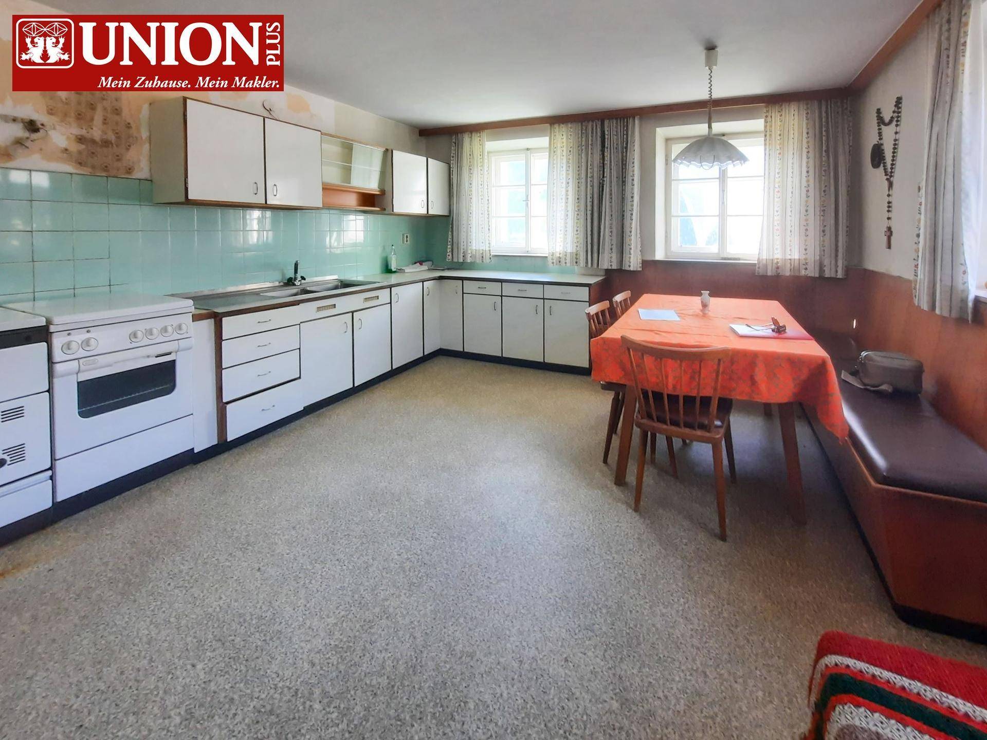 Geräumige Küche im älteren Stil mit weißen Schränken, hellblauen Fliesen und einem Essbereich am Fenster.