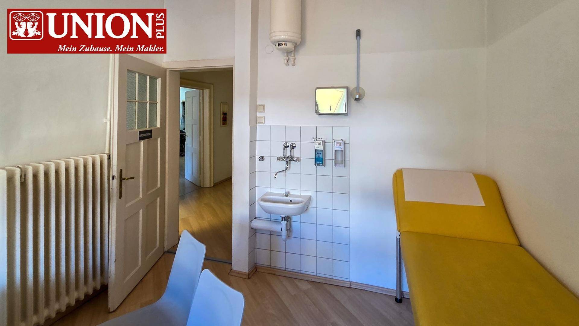 Behandlungszimmer mit Waschbecken, gefliester Wand, Heizkörper und gelber Untersuchungsliege.