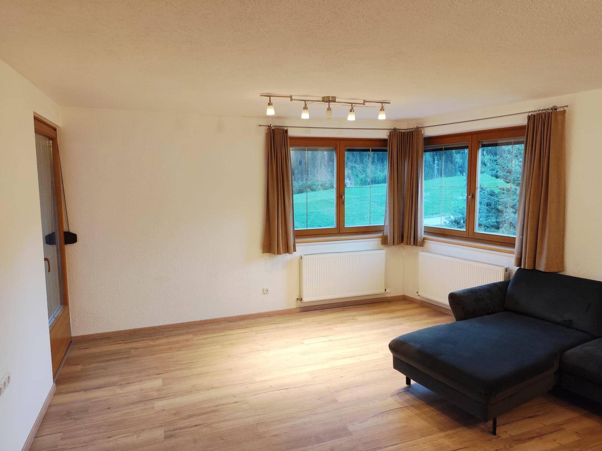 Helles Wohnzimmer mit Laminatboden, gemütlichem Sofa und großen Fenstern mit Blick ins Grüne.