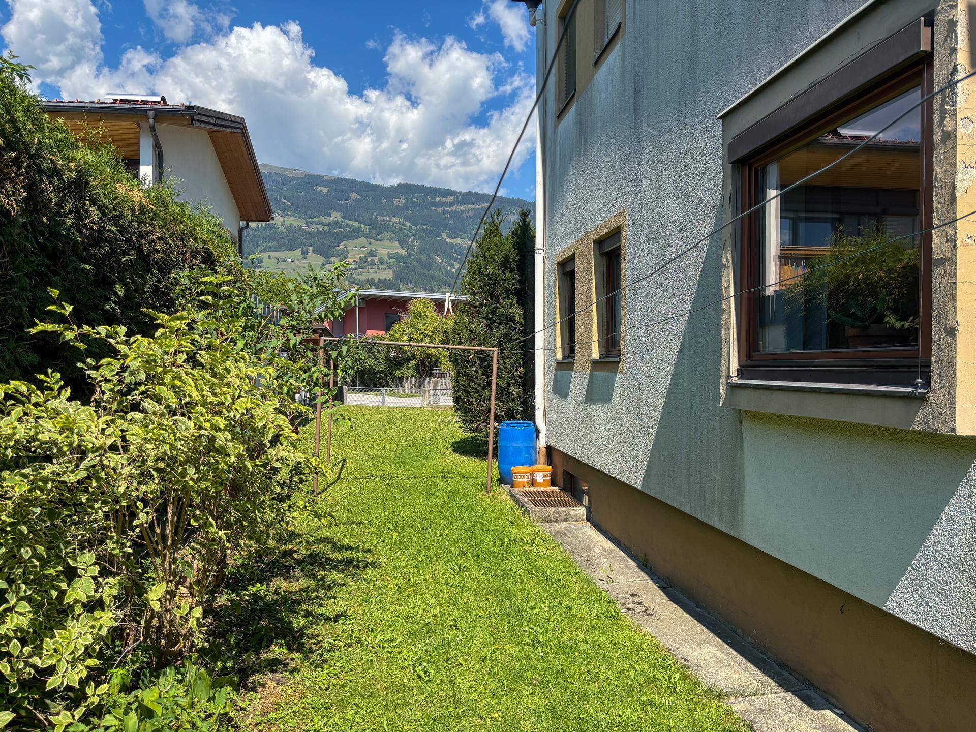 Seitlicher Gartenbereich mit Rasenfläche und Blick auf die bewaldeten Hügel im Hintergrund.