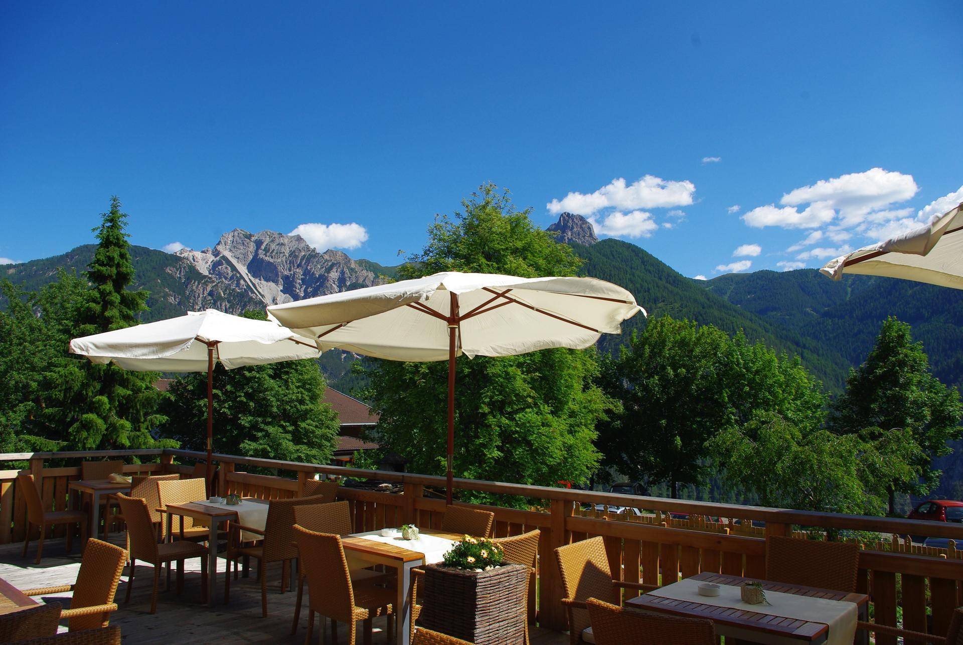 Geräumige Terrasse mit Tischen, Stühlen und Sonnenschirmen, die einen atemberaubenden Blick auf die Berge bietet.