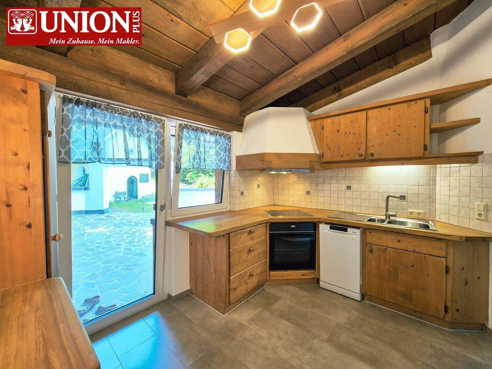 Rustikale Holzküche mit Einbaugeräten, Fliesenboden und direktem Zugang zum Außenbereich.