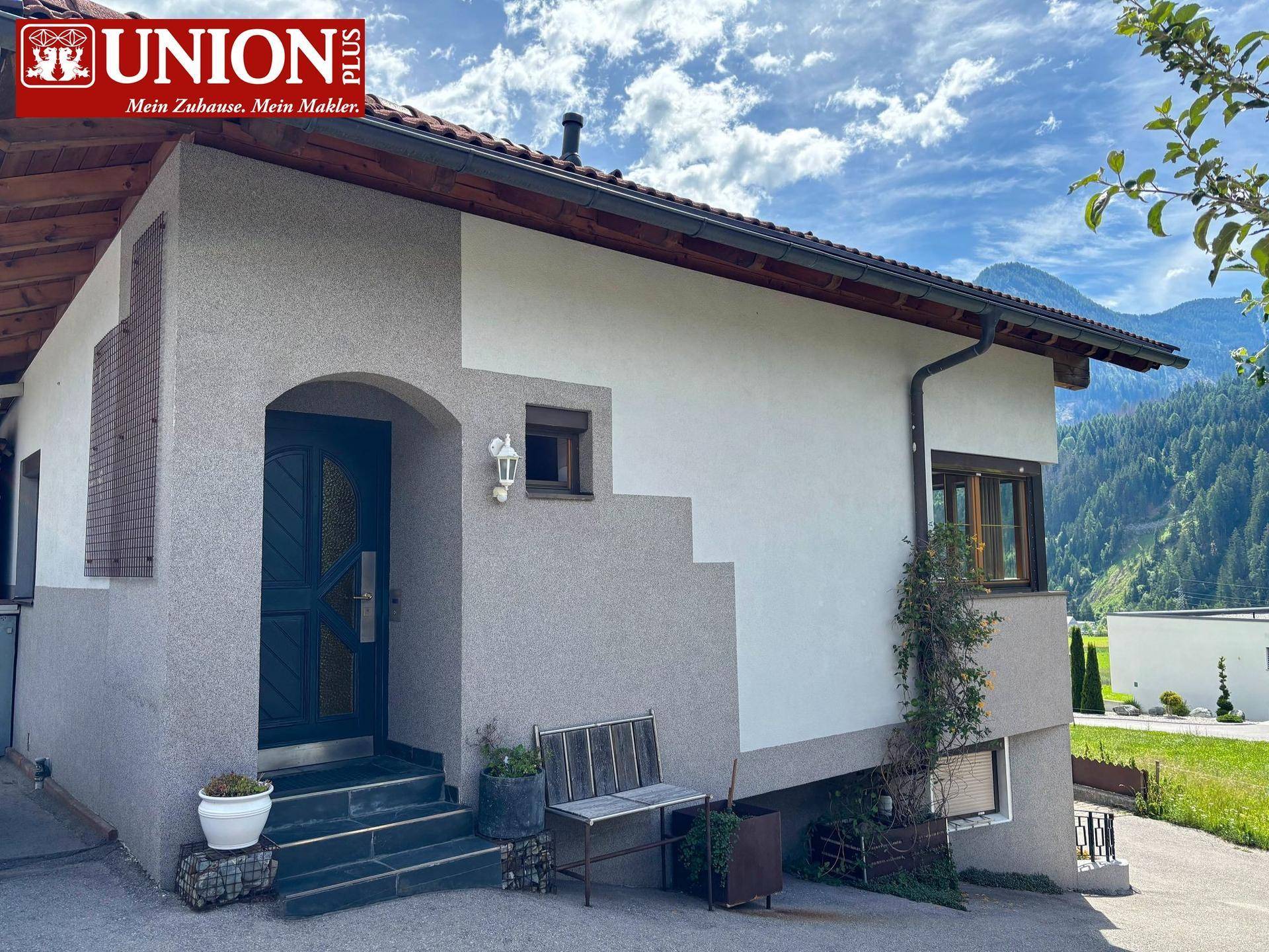 Eingangsbereich eines Hauses mit traditioneller Architektur, Fensterläden und einem kleinen Sitzbereich im Freien.