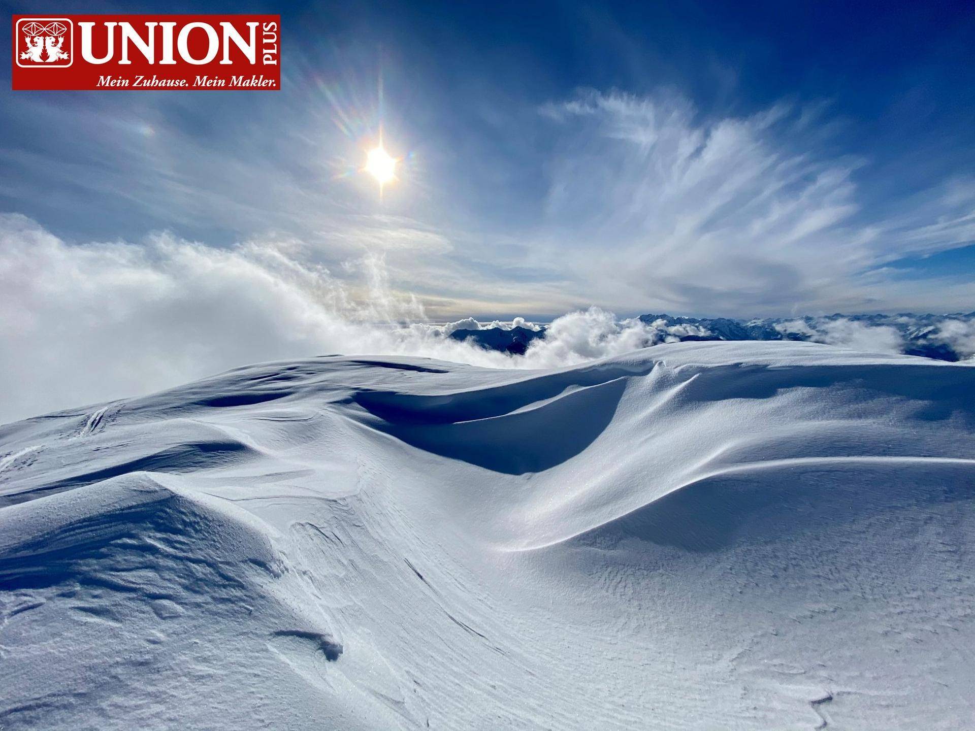 Atemberaubender Blick auf schneebedeckte Berggipfel über den Wolken unter strahlendem Sonnenschein.