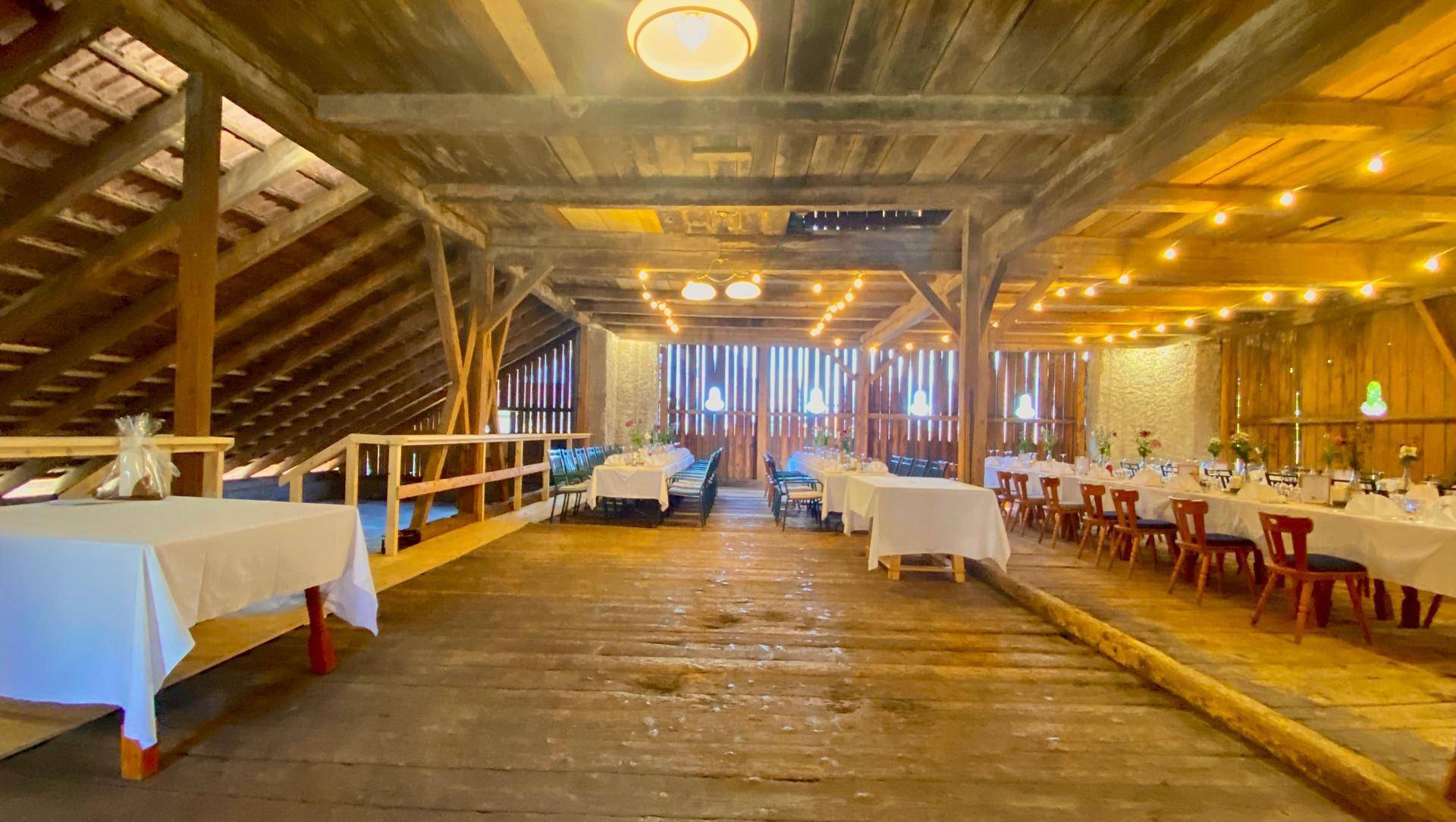 Geräumiger Veranstaltungsraum mit Holzboden, sichtbaren Dachbalken und festlicher Dekoration für Veranstaltungen.