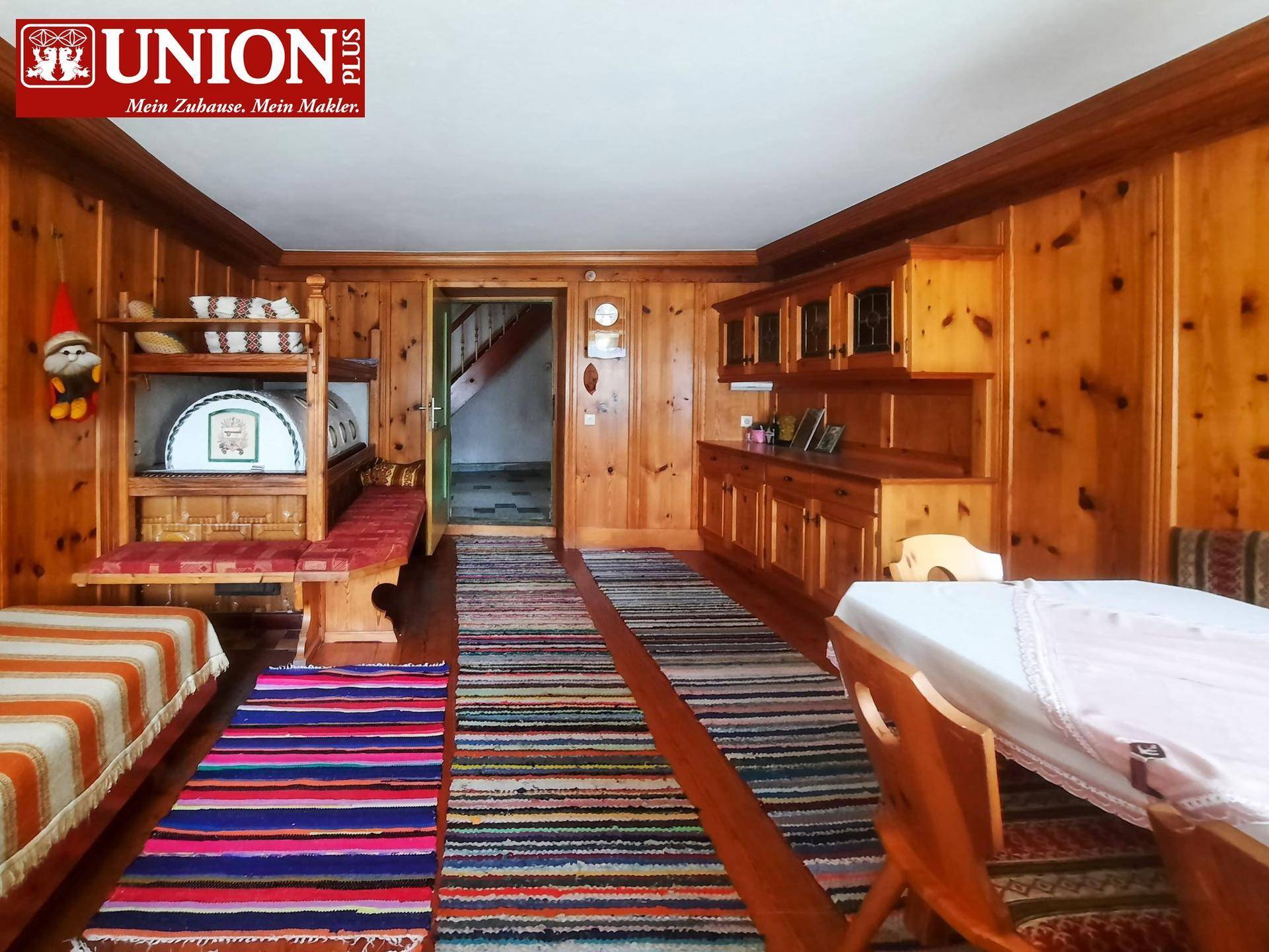 Gemütlicher Wohn- und Essbereich mit umfangreicher Holzvertäfelung, bunten Teppichen und traditionellen Möbeln.