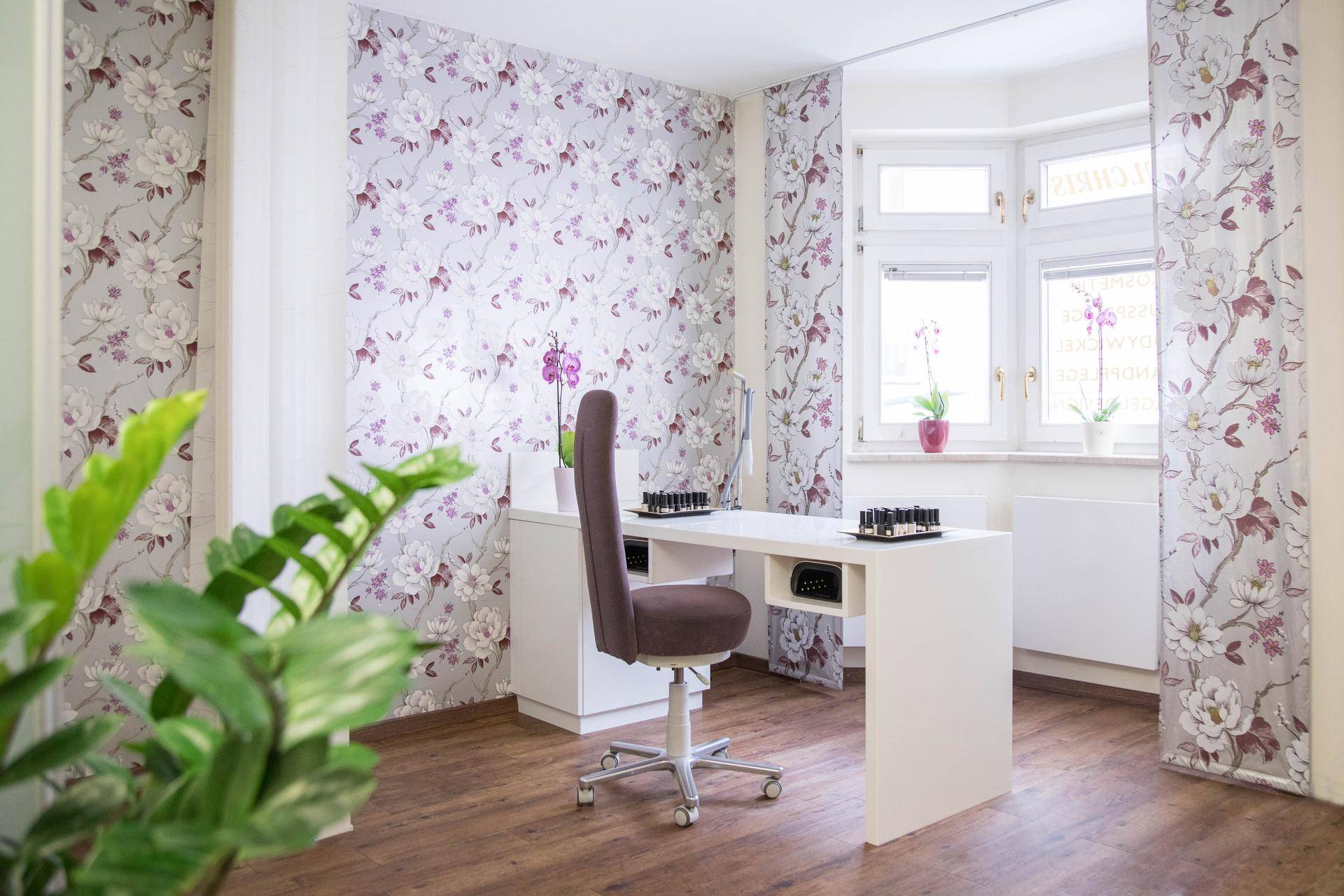 Modern gestalteter Geschäftsraum mit floraler Tapete, hellem Laminatboden und viel Tageslicht durch die Fensterfront.
