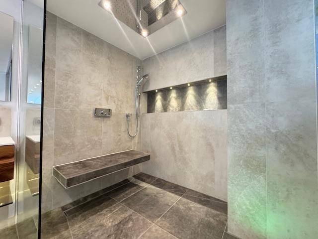 Elegante begehbare Dusche mit Regenduschkopf, Fliesen und integrierter Sitzbank.
