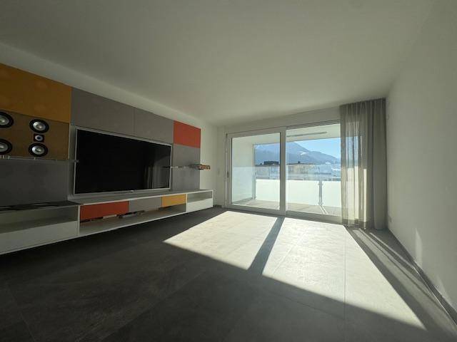Moderner Wohnbereich mit großem Fernseher, Medieneinheit und sonnigem Zugang zum Balkon mit Bergblick.