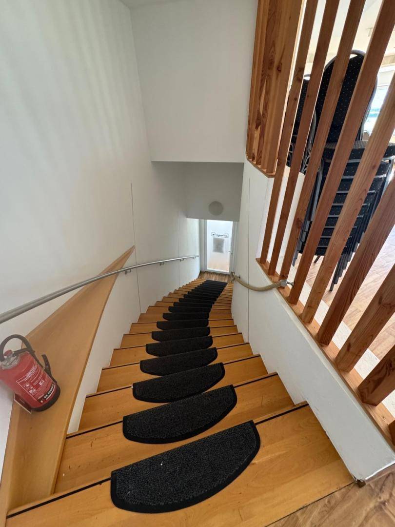 Holztreppe mit schwarzem Teppichläufer und Holzgeländer, führt in ein unteres Stockwerk.