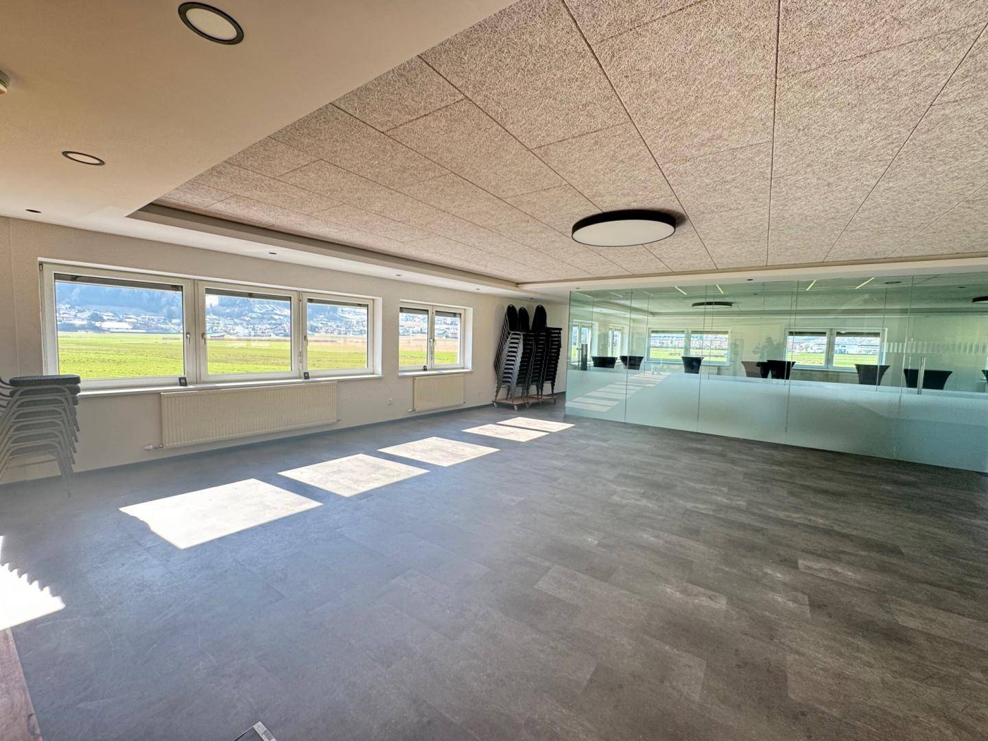 Geräumiger Konferenzraum mit Fliesenboden, Glasabtrennung und weitem Blick auf die grüne Landschaft.