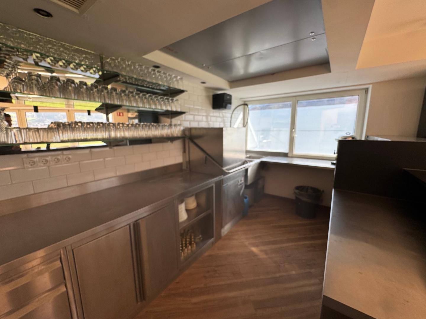 Professionelle Küche oder Bar mit Edelstahltheken, Glasregalen und einem Fenster mit Ausblick.
